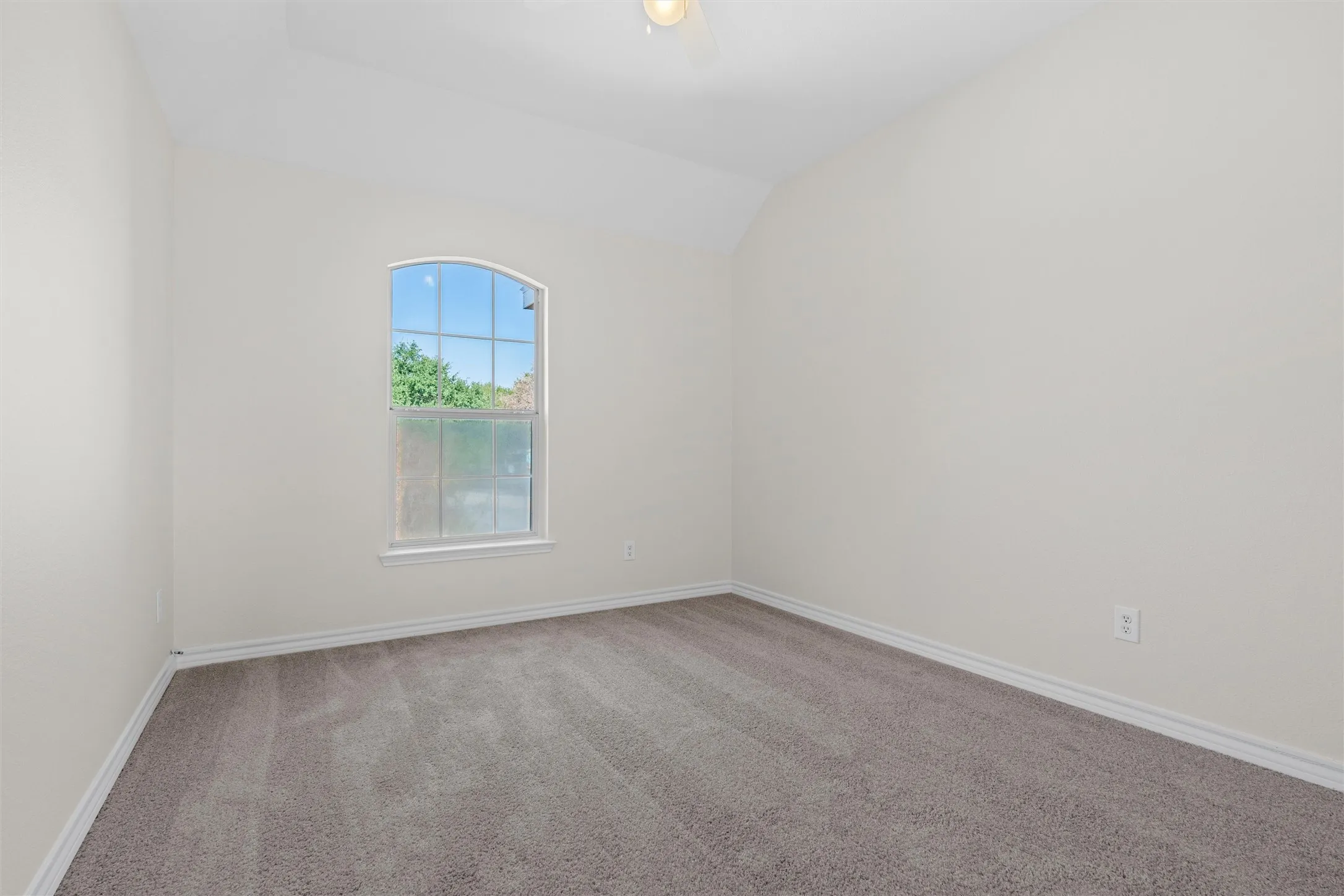 Arched window with exterior views, vaulted ceiling, neutral wall color, and grey carpet flooring
