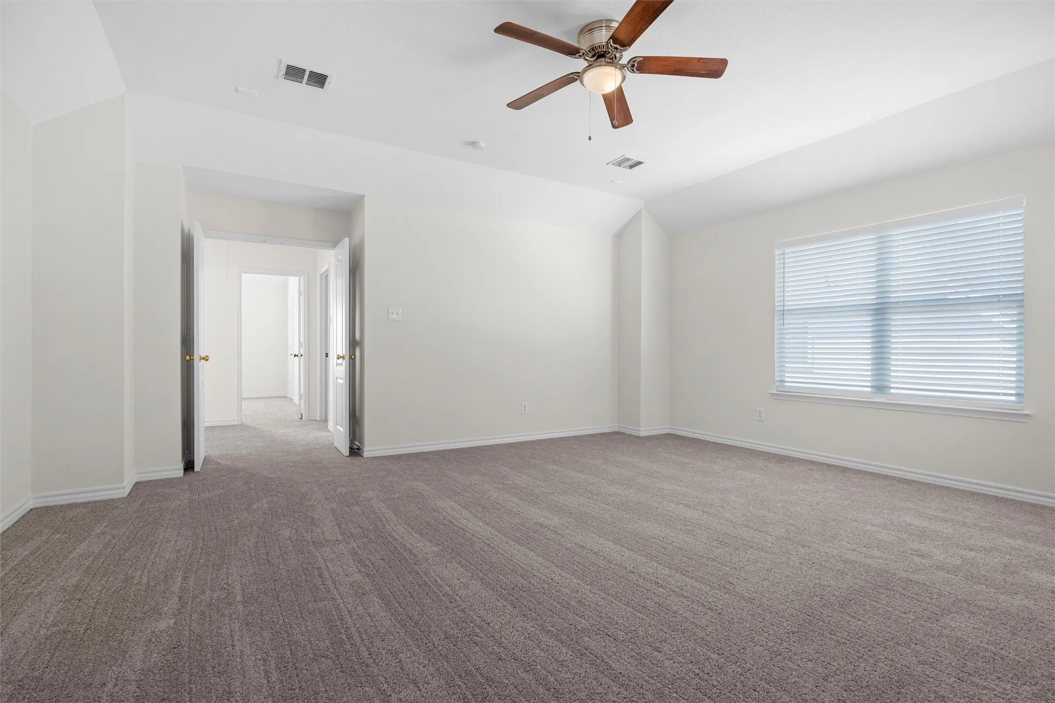 Spacious room with plush carpeting, a large window, a ceiling fan with integrated lighting, and multiple interior doorways