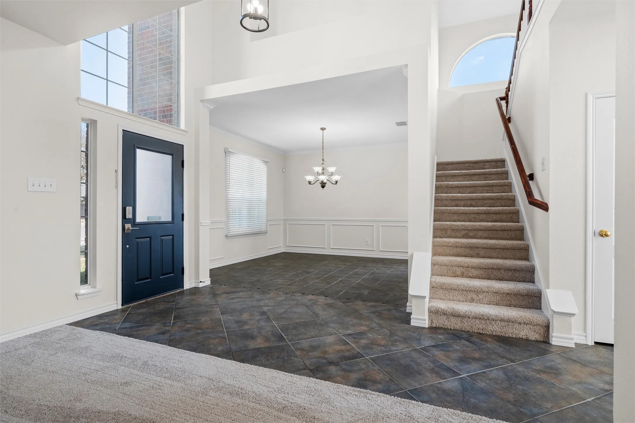 Two-story foyer with high ceilings, dark tile flooring, and an arched transom window