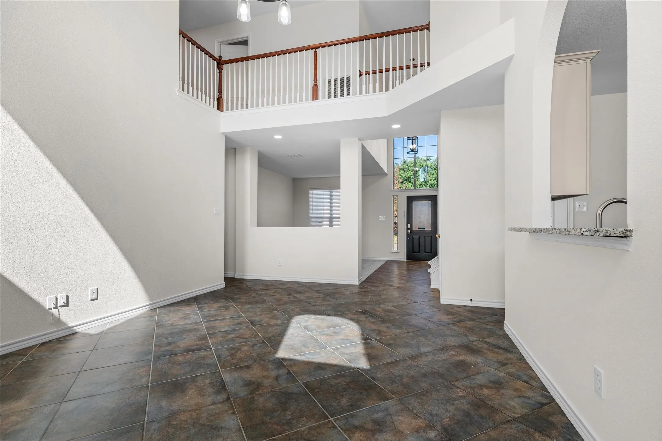 Two-story living space featuring high ceilings, tile flooring, and an open upper-level landing with wood and white balusters