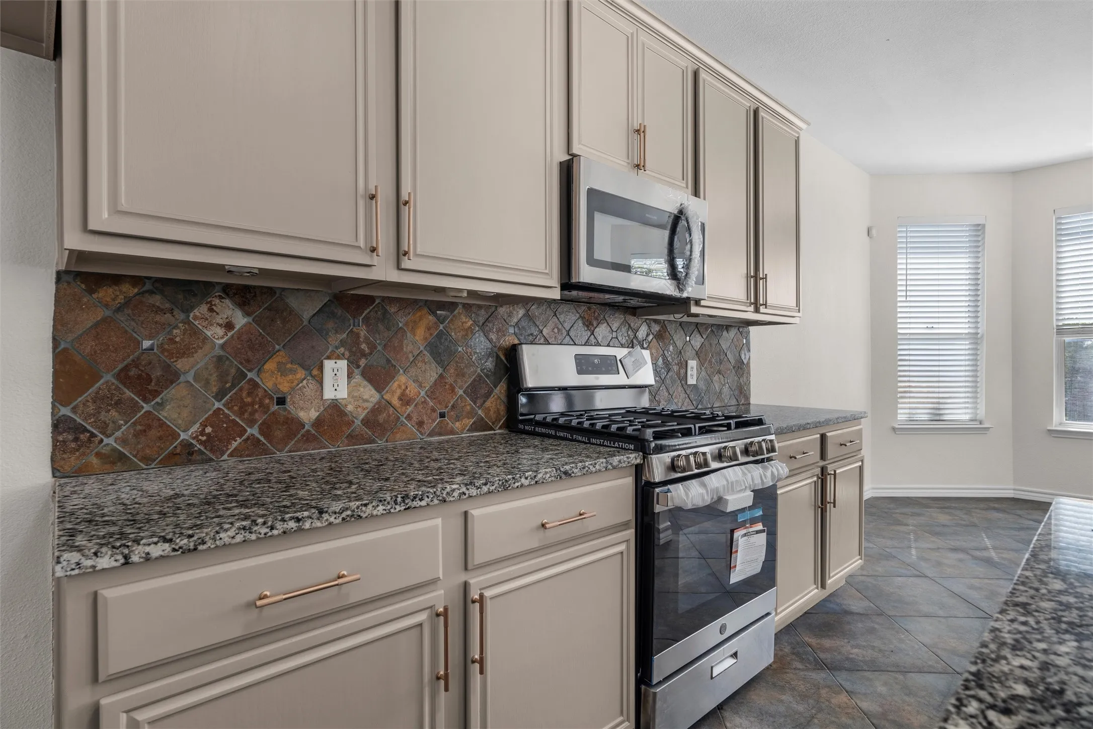 Kitchen featuring granite-style countertops, under-cabinet lighting, stainless steel appliances, a gas range, and a tiled backsplash