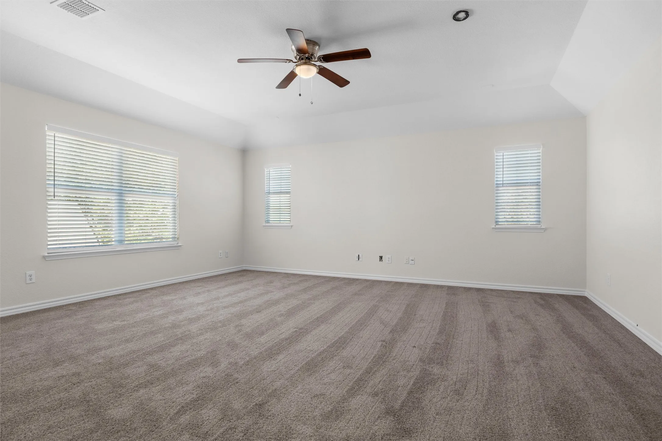 Expansive room featuring vaulted ceilings, a ceiling fan with integrated lighting, recessed lighting, two windows with blinds, and neutral carpeting