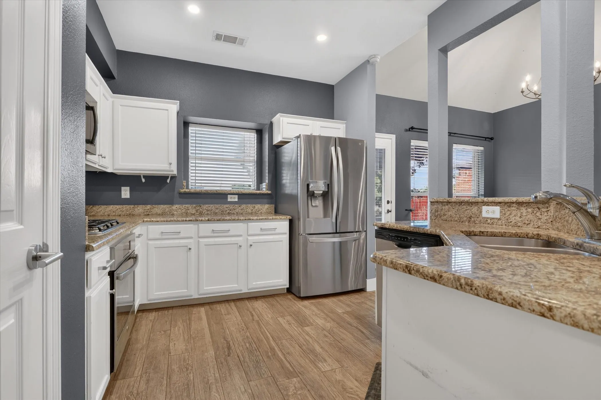 Kitchen featuring white cabinetry, stone countertops, stainless steel appliances, and wood-finish flooring
