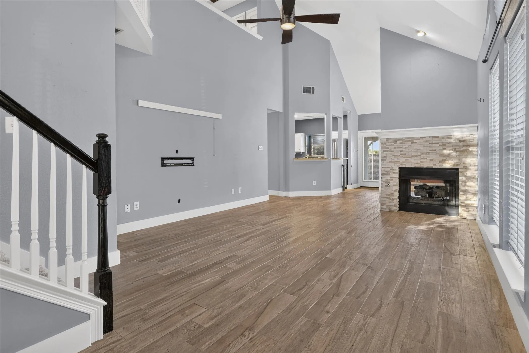 Vaulted ceilings, wood-finish flooring, stone-surround fireplace, ceiling fan, and wooden staircase railing