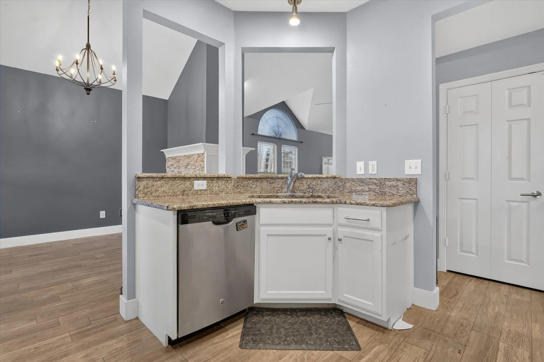 Kitchen area featuring wood-finish flooring, white cabinetry, stone-finish countertops, stainless steel dishwasher, and metal-finish faucet