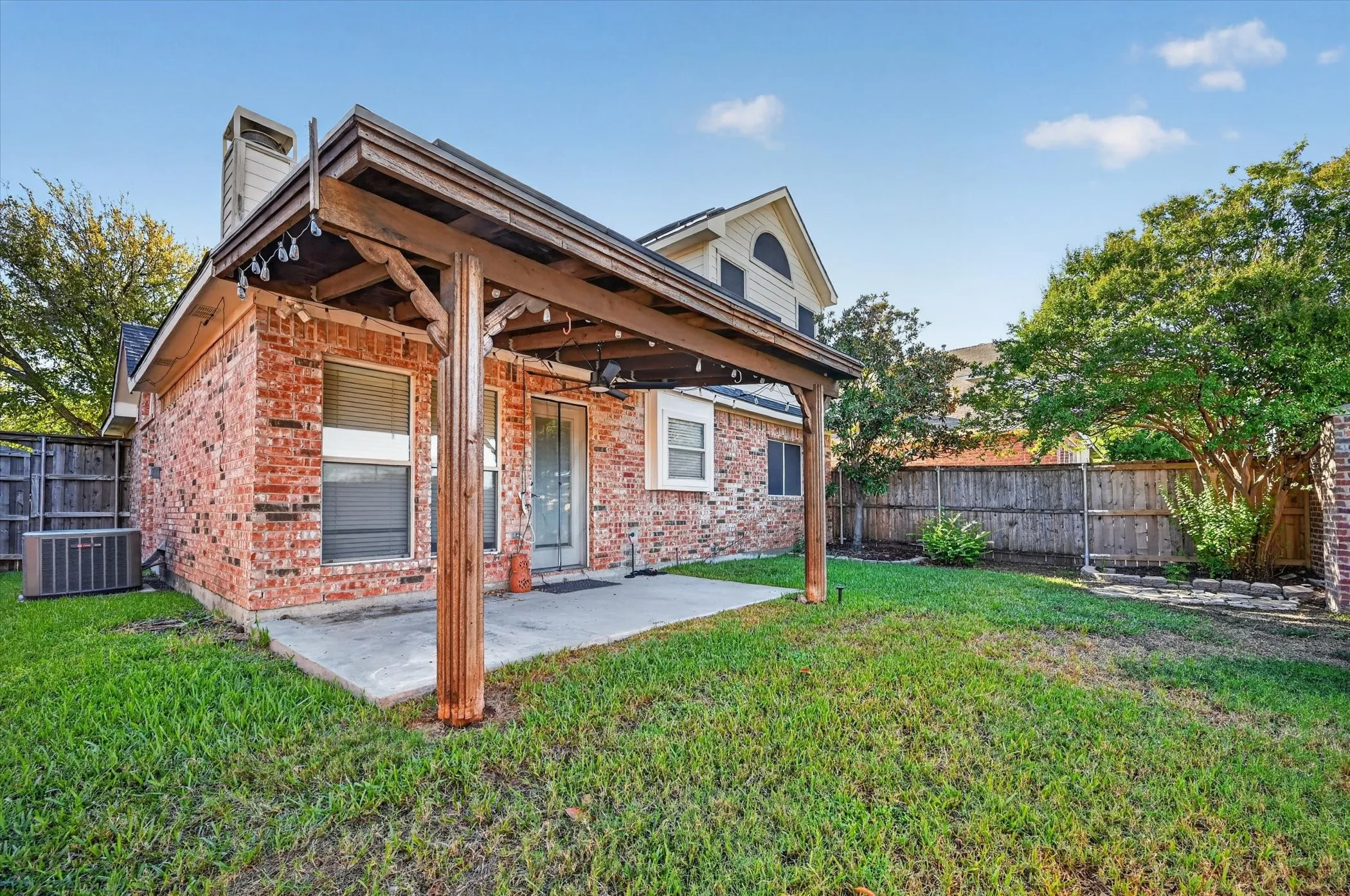 Rear brick elevation with a covered patio, concrete slab, wood privacy fencing, and a mature tree