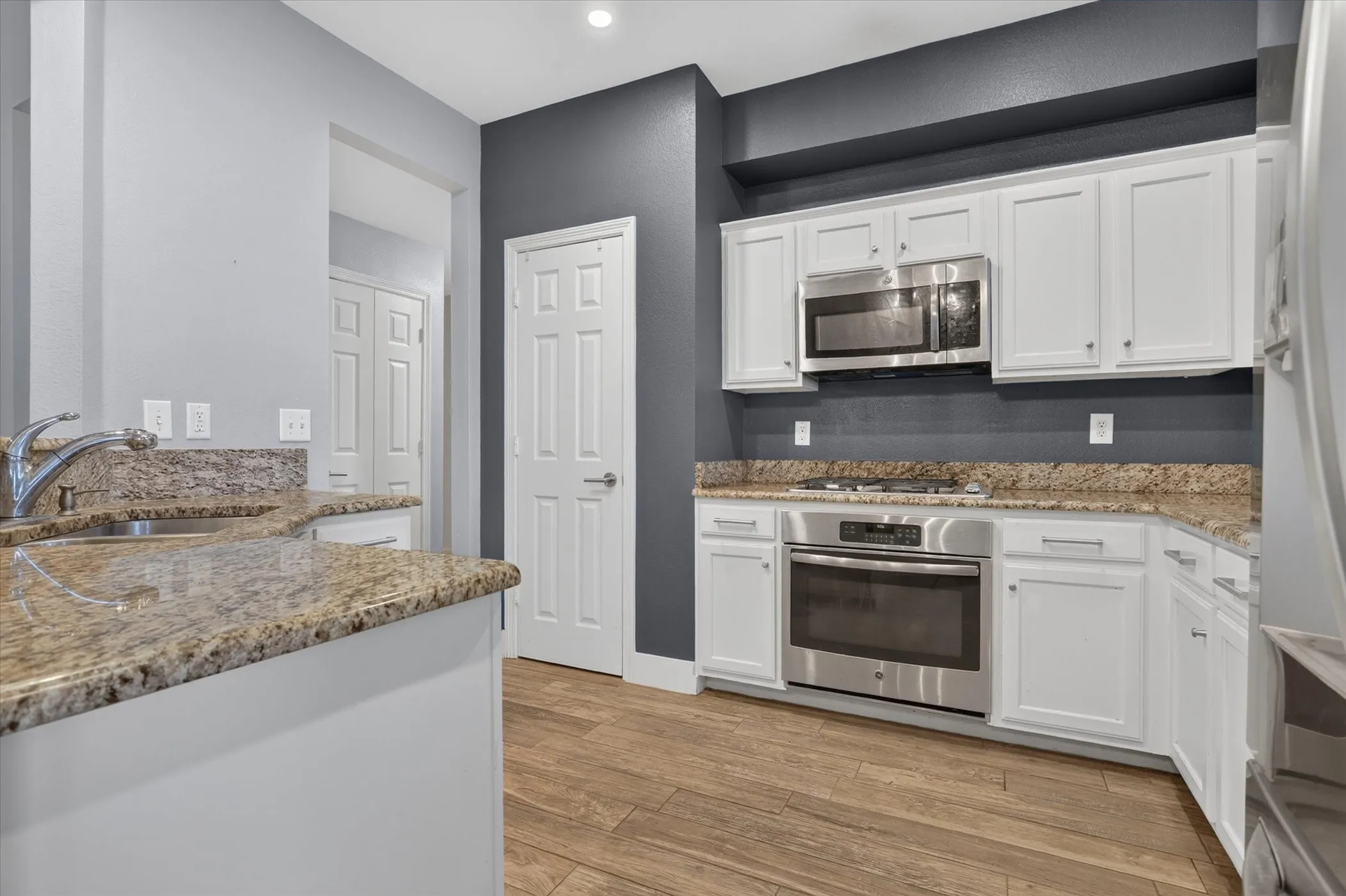 Kitchen featuring white cabinetry, stone-surface countertops, wood-finish flooring, and built-in stainless steel appliances