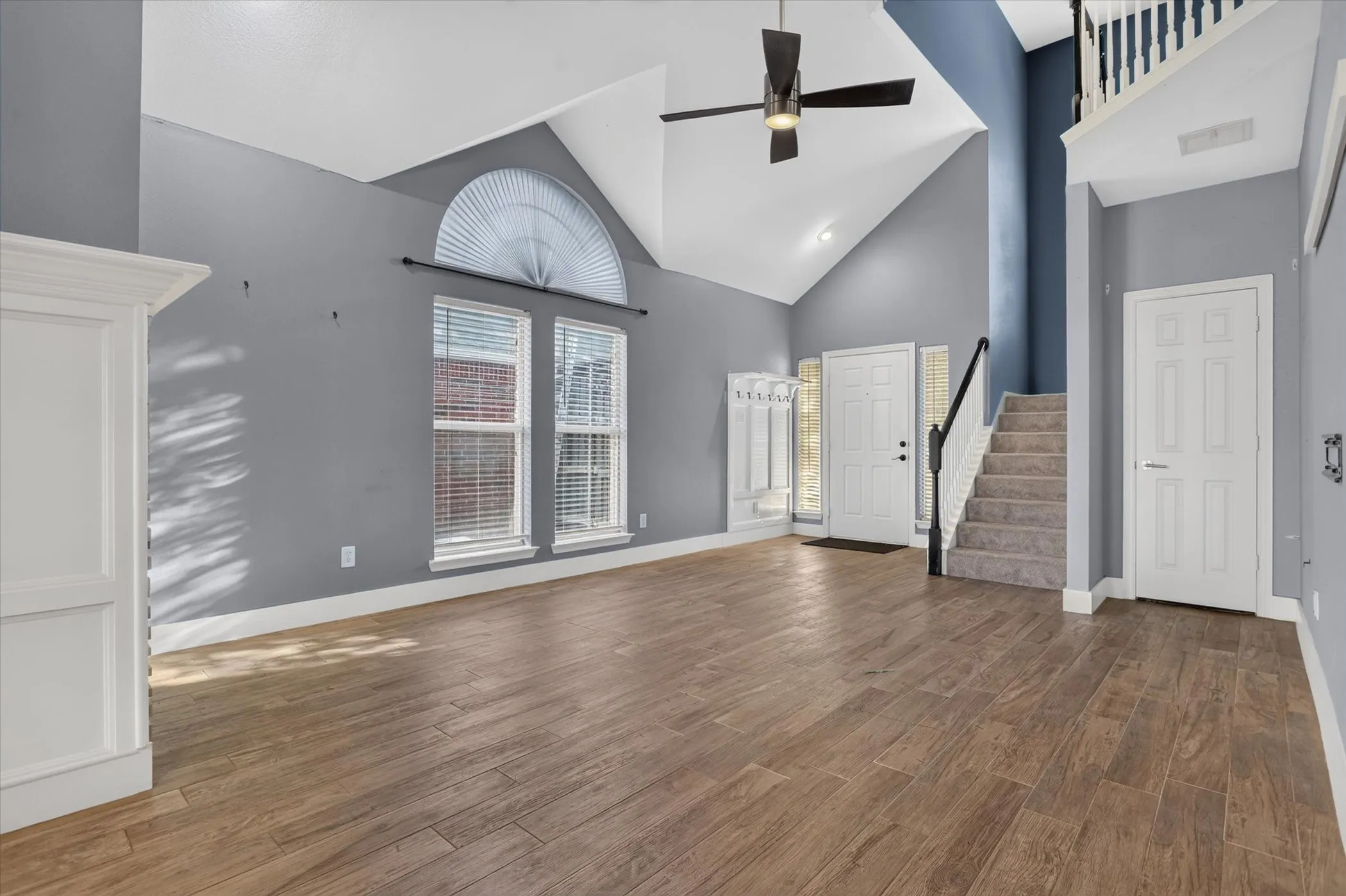 Vaulted ceilings with an arched transom window, wood-finish flooring, and a ceiling fan with integrated lighting