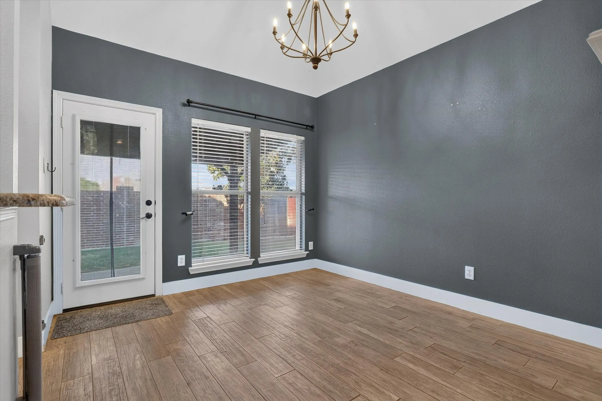Vaulted ceilings, wood-finish flooring, charcoal-toned walls, decorative metal chandelier, and full-light exterior door