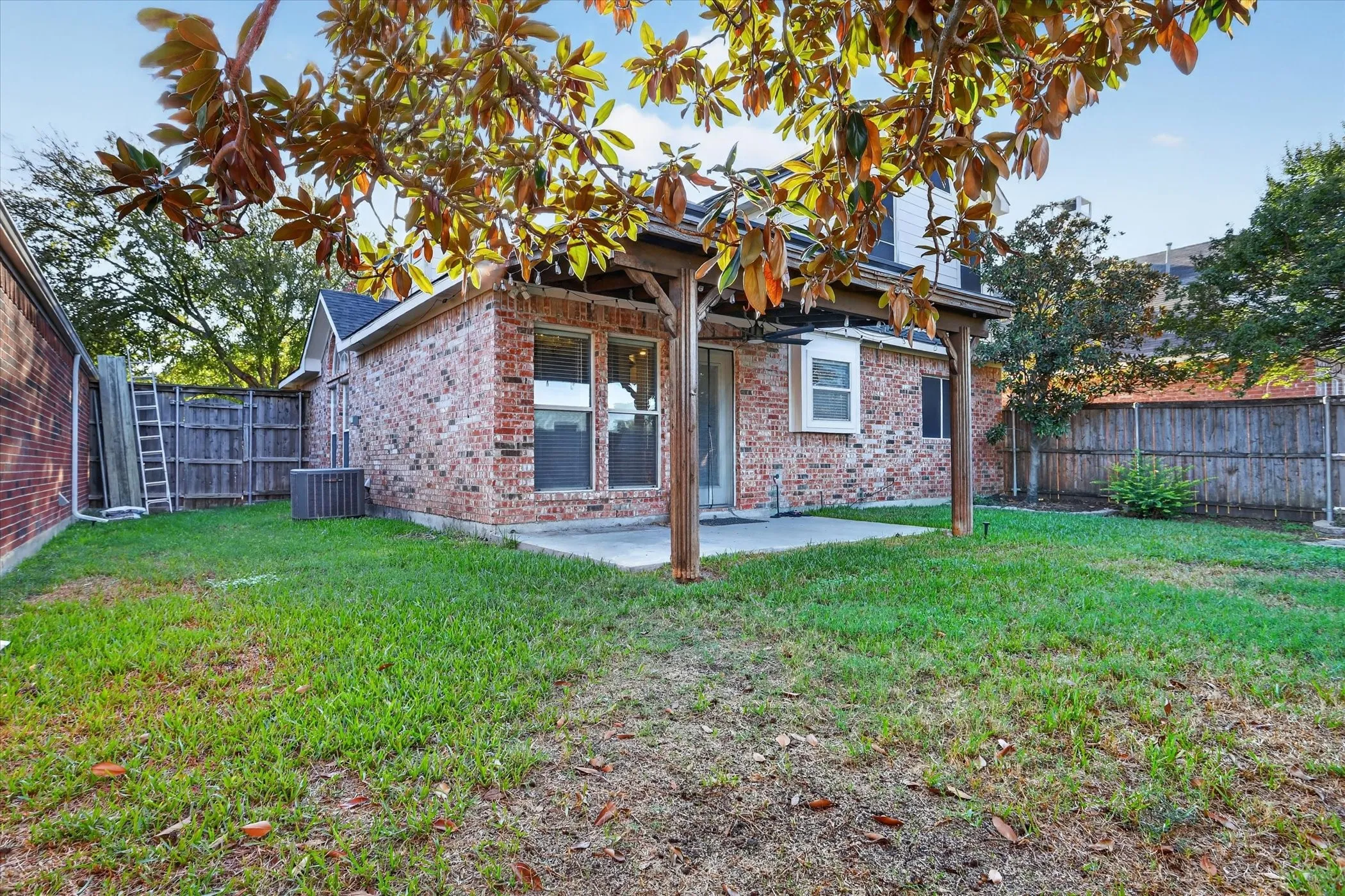 Brick exterior featuring a covered patio with wood support beams, concrete flooring, and a fenced backyard