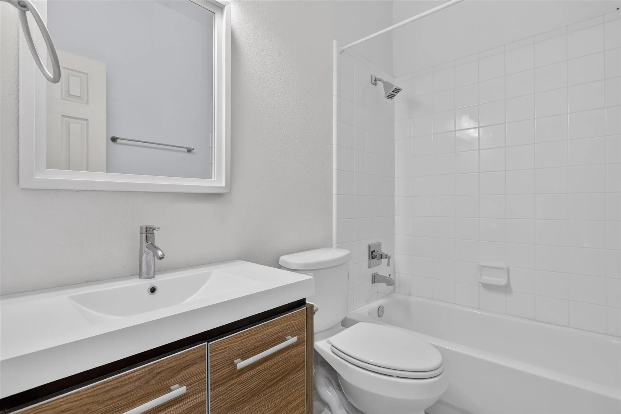 Bathroom featuring a vanity with a wood-finish cabinet and integrated sink, a framed wall mirror, a ceramic tile tub surround, and polished chrome fixtures