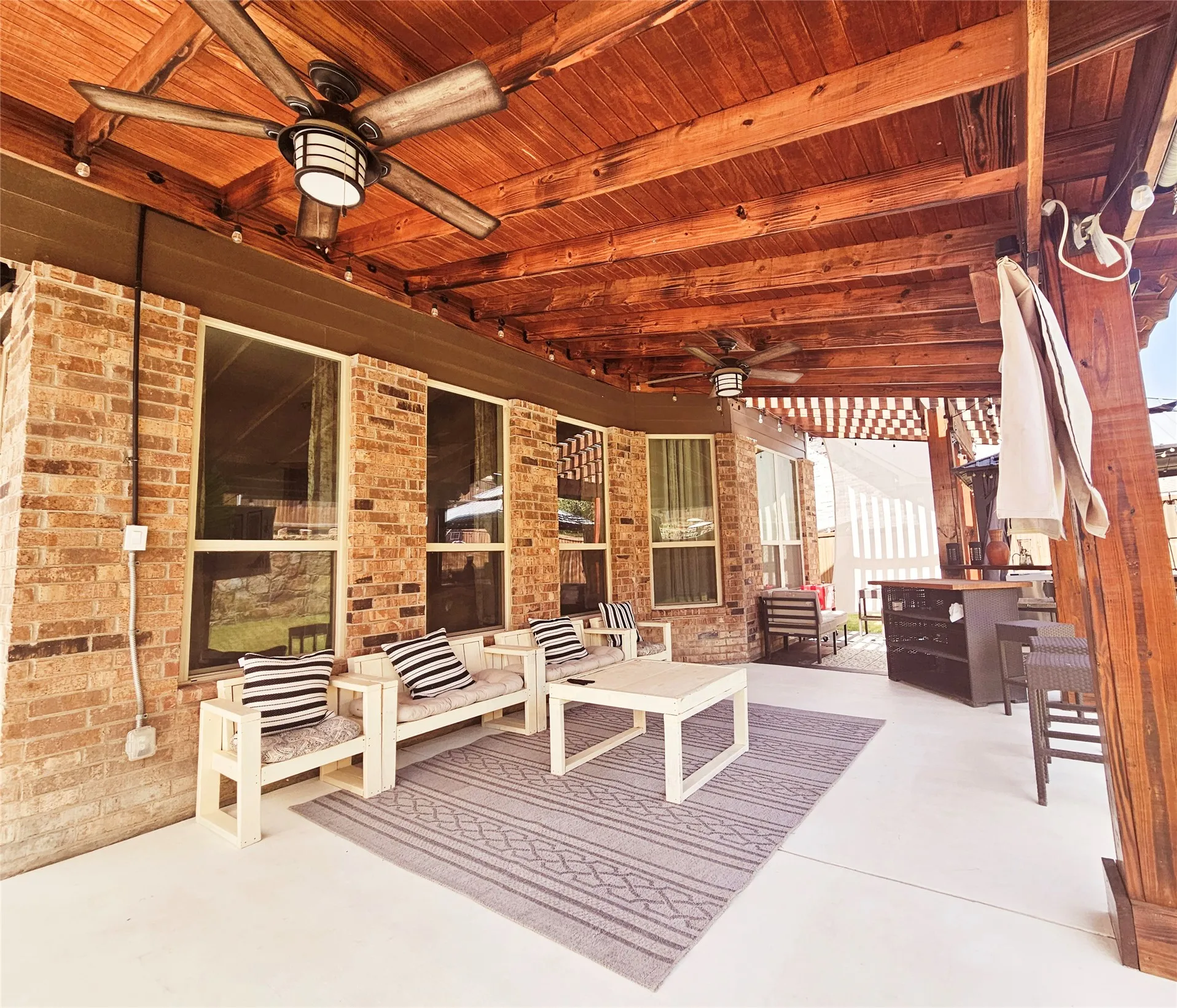 Covered outdoor patio with a wood plank ceiling, exposed wood beams, and a brick exterior
