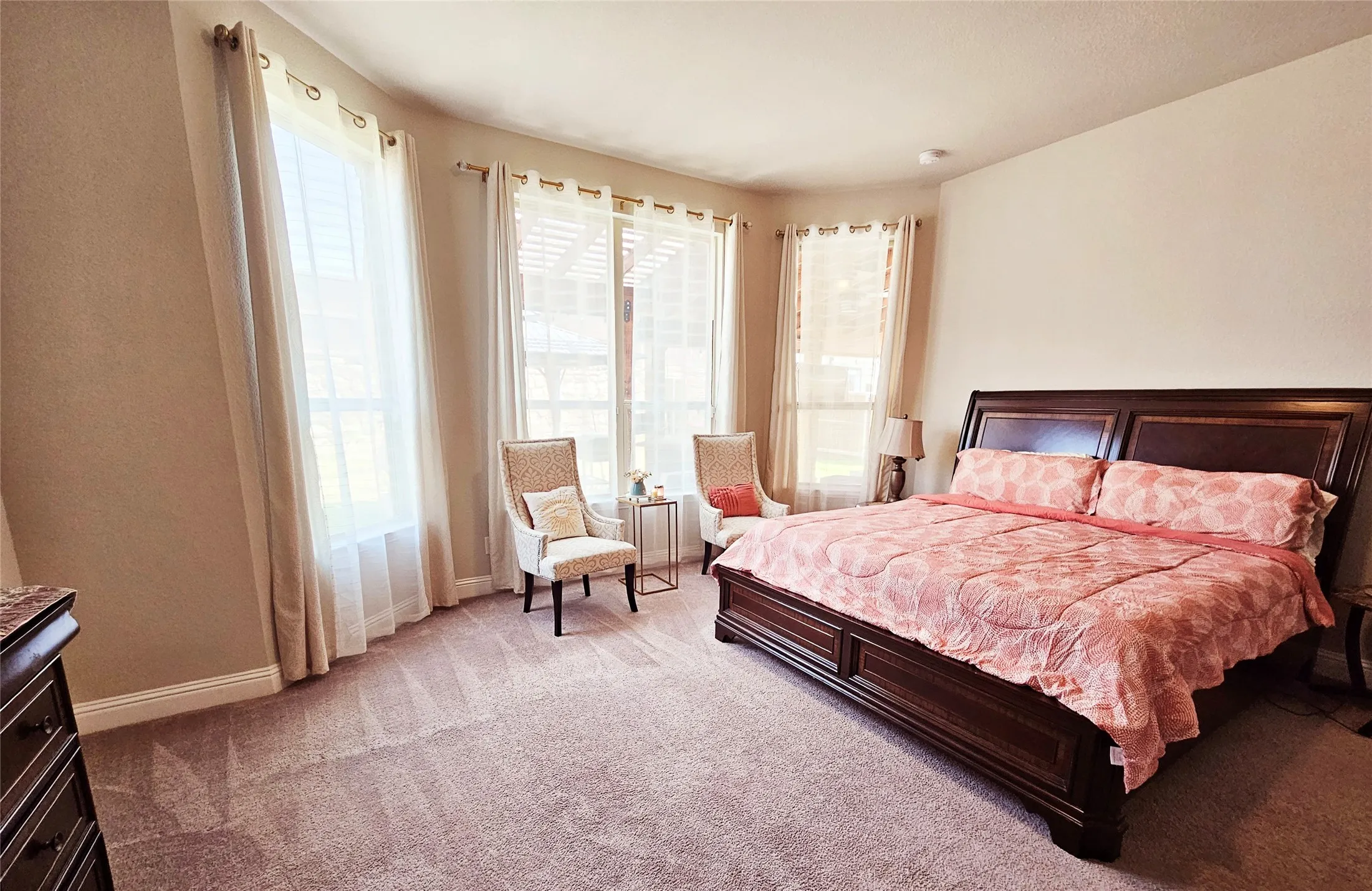 Carpeted flooring with a prominent bay window area, featuring multiple windows with drapery rods and sheer privacy coverings