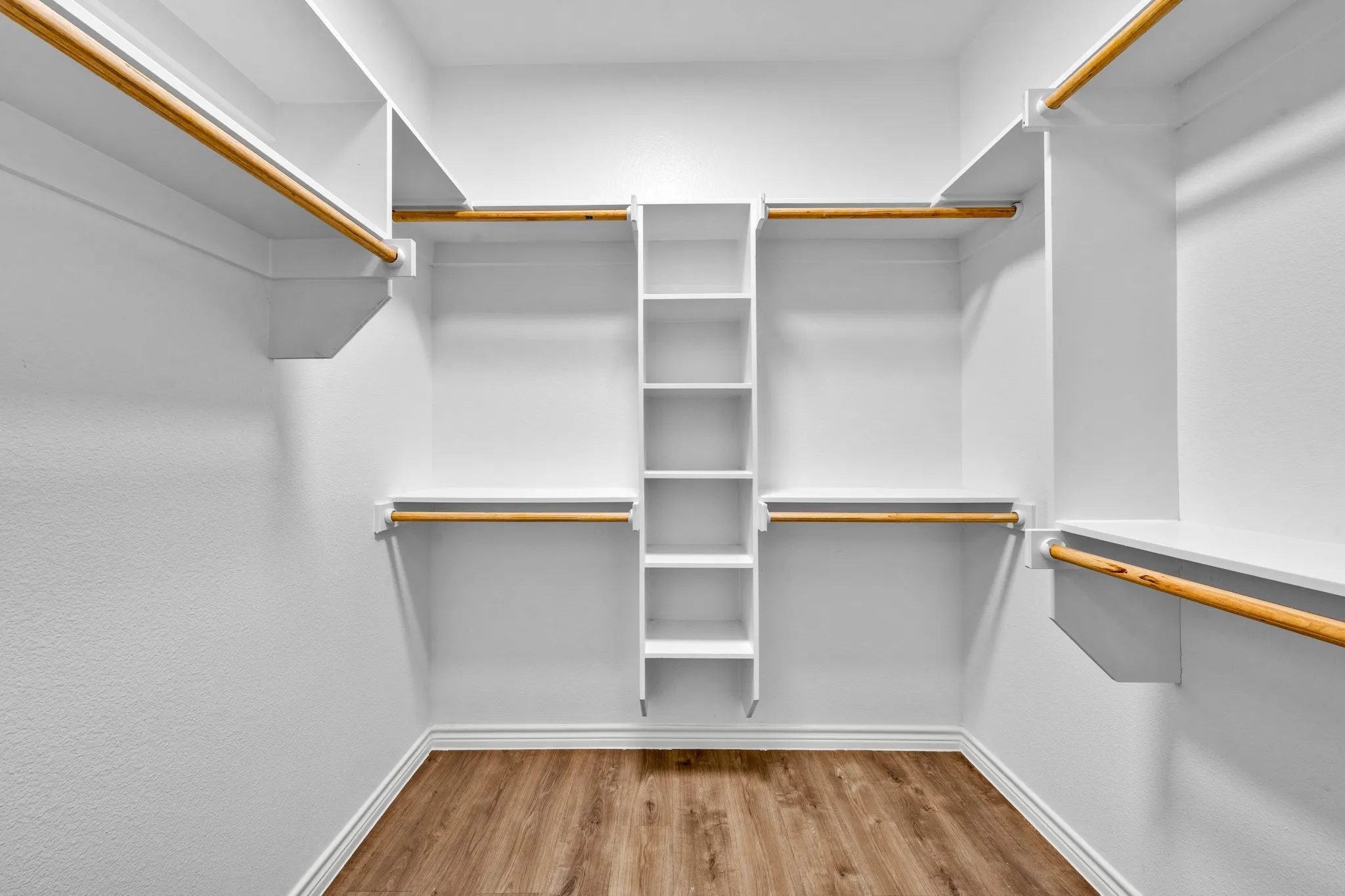 Walk-in closet with wood-finish flooring, white built-in shelving, multiple hanging rods, and painted white walls