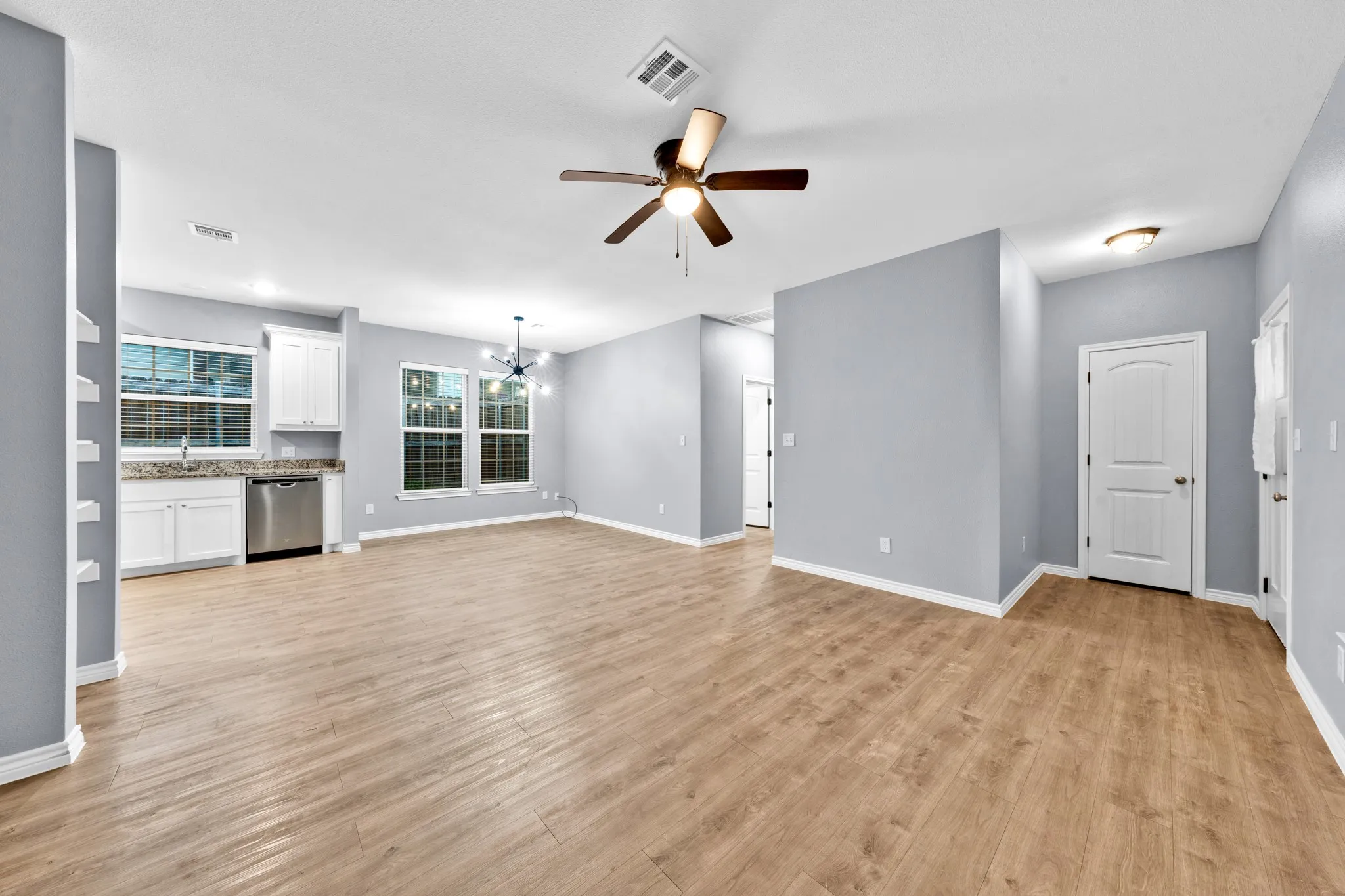 Wood-finish flooring, white cabinetry, integrated stainless steel dishwasher, ceiling fan, and modern chandelier