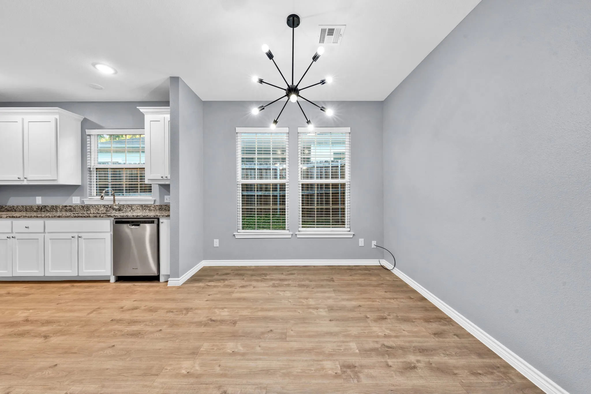 Wood-finish flooring throughout, white cabinetry, stainless steel dishwasher, and a contemporary chandelier