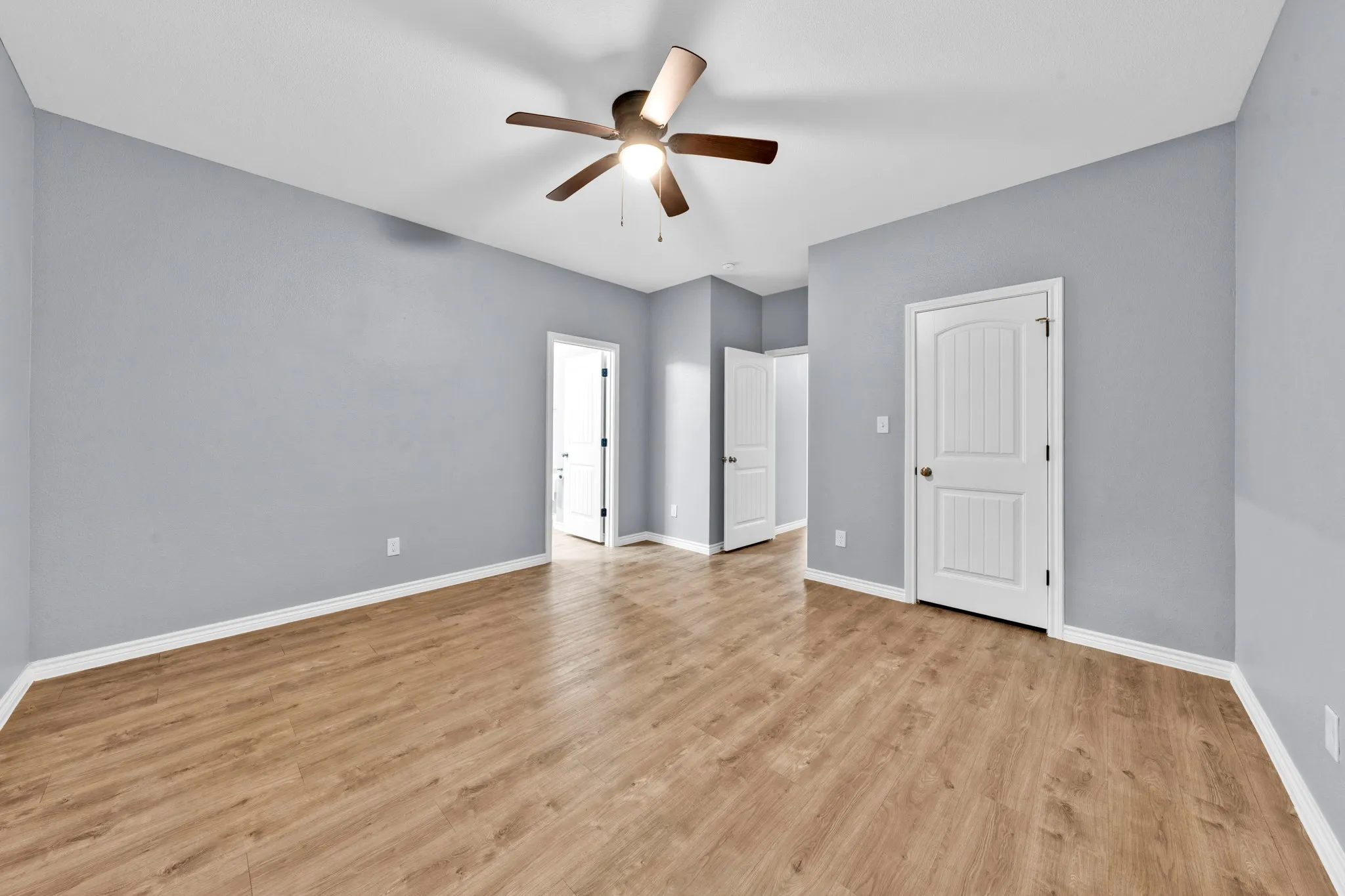 Spacious room featuring wood-finish flooring, light grey walls, white trim, and a ceiling fan