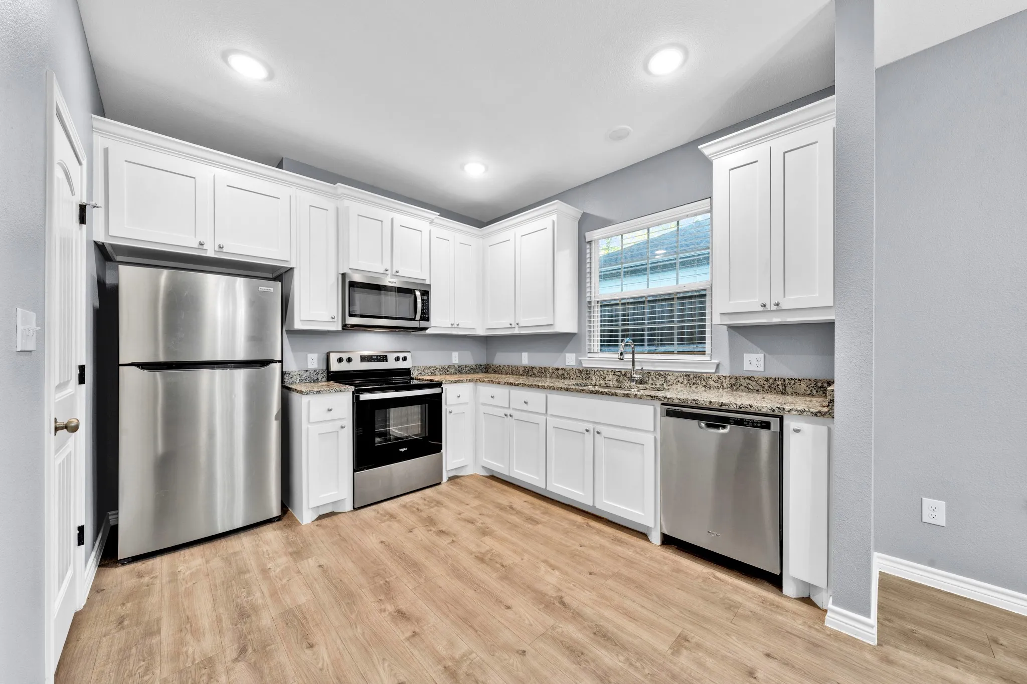 Kitchen featuring white shaker cabinetry, stainless steel appliances, wood-finish flooring, recessed lighting, and granite-style countertops