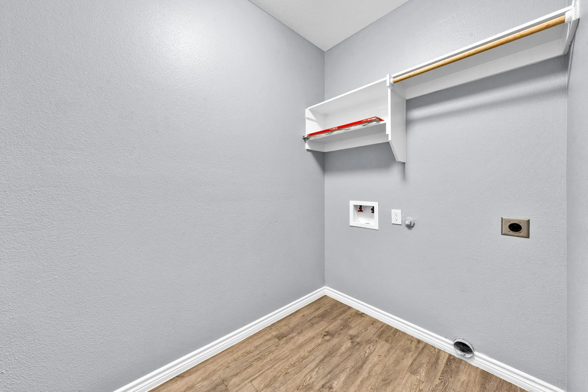Dedicated laundry area featuring wood-finish flooring, white trim, and built-in shelving with a hanging rod