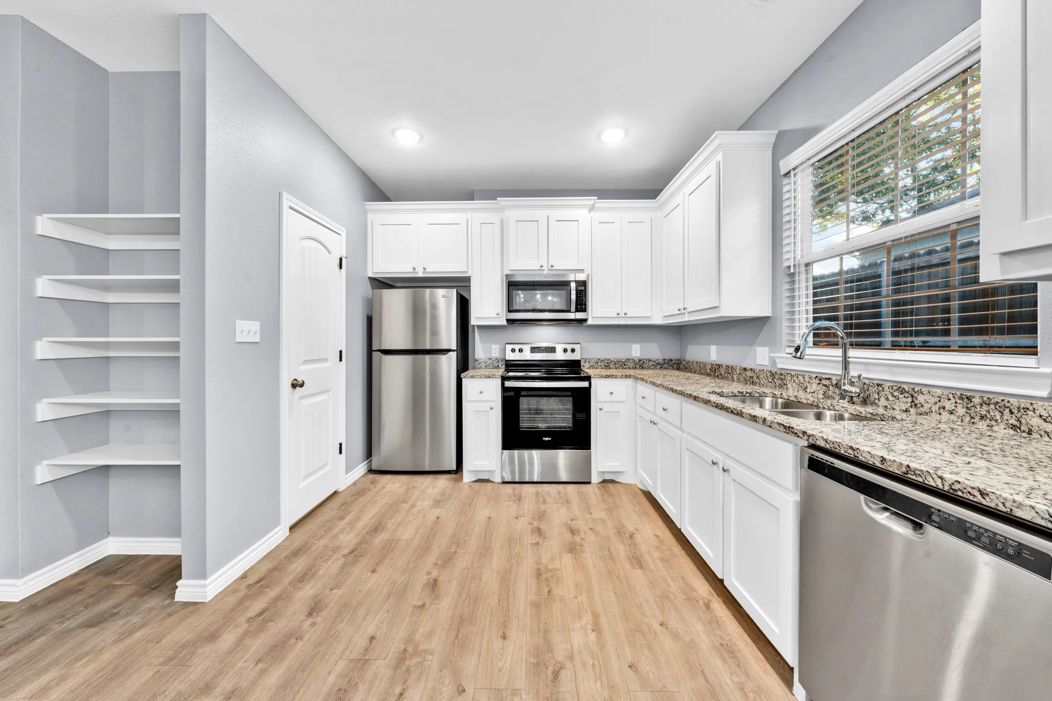 Kitchen featuring stainless steel appliances, wood-finish flooring, white cabinetry, a double basin sink, and ample counter space