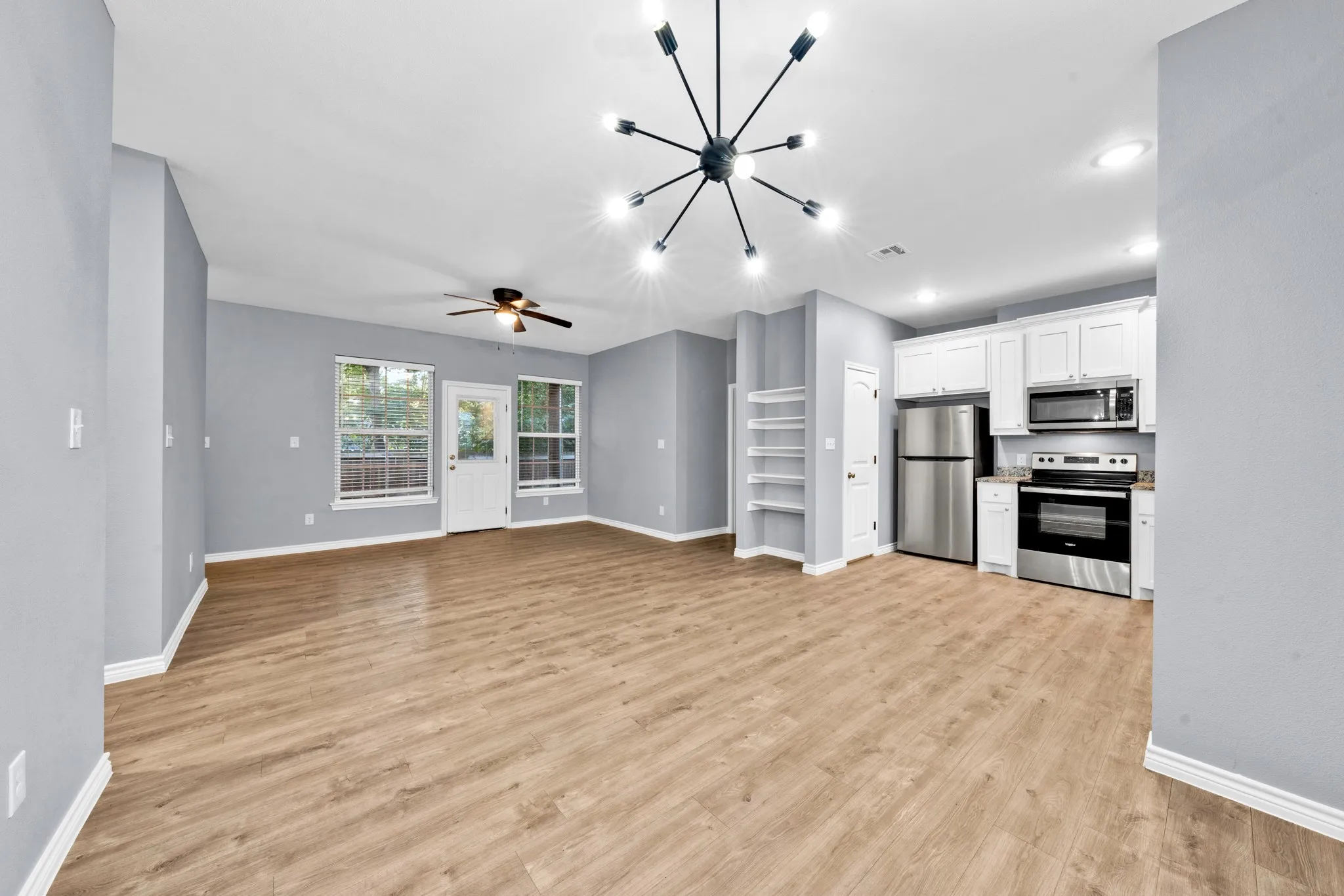 Open-concept living space with wood-finish flooring, white cabinetry, stainless steel appliances, and a modern light fixture