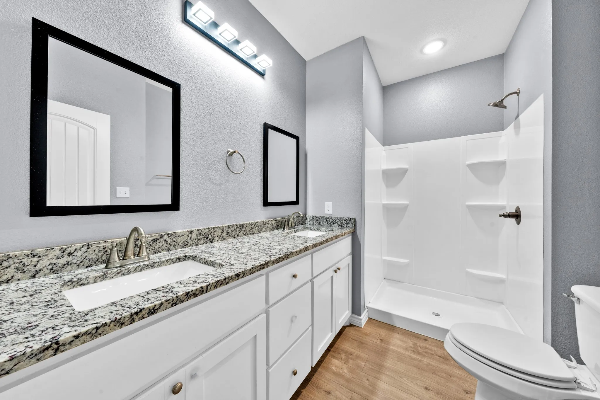 Dual vanity with granite countertop, integrated sinks, white cabinetry, and wood-finish flooring
