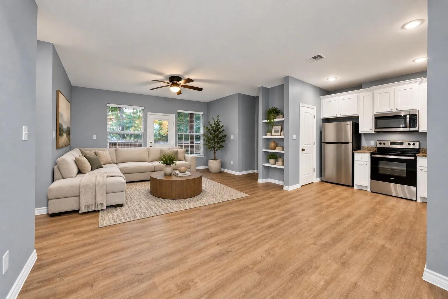 Open-concept living area with wood-finish flooring, a ceiling fan, and multiple windows