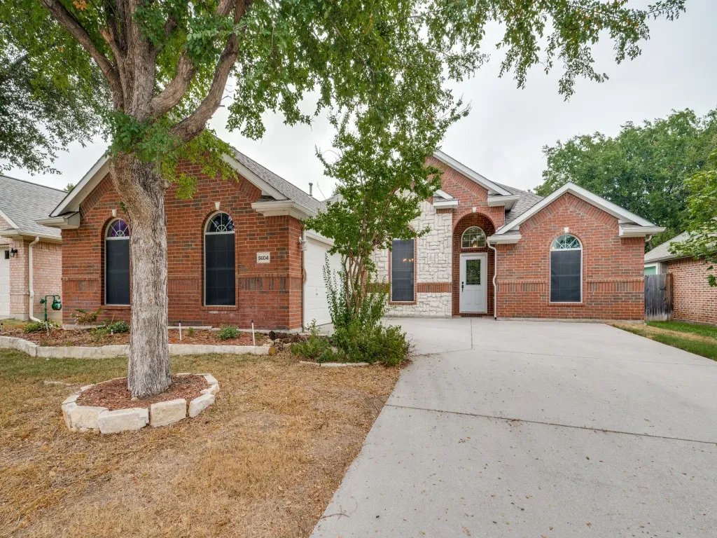 Brick and stone exterior with arched windows, a front entry door, and a concrete driveway