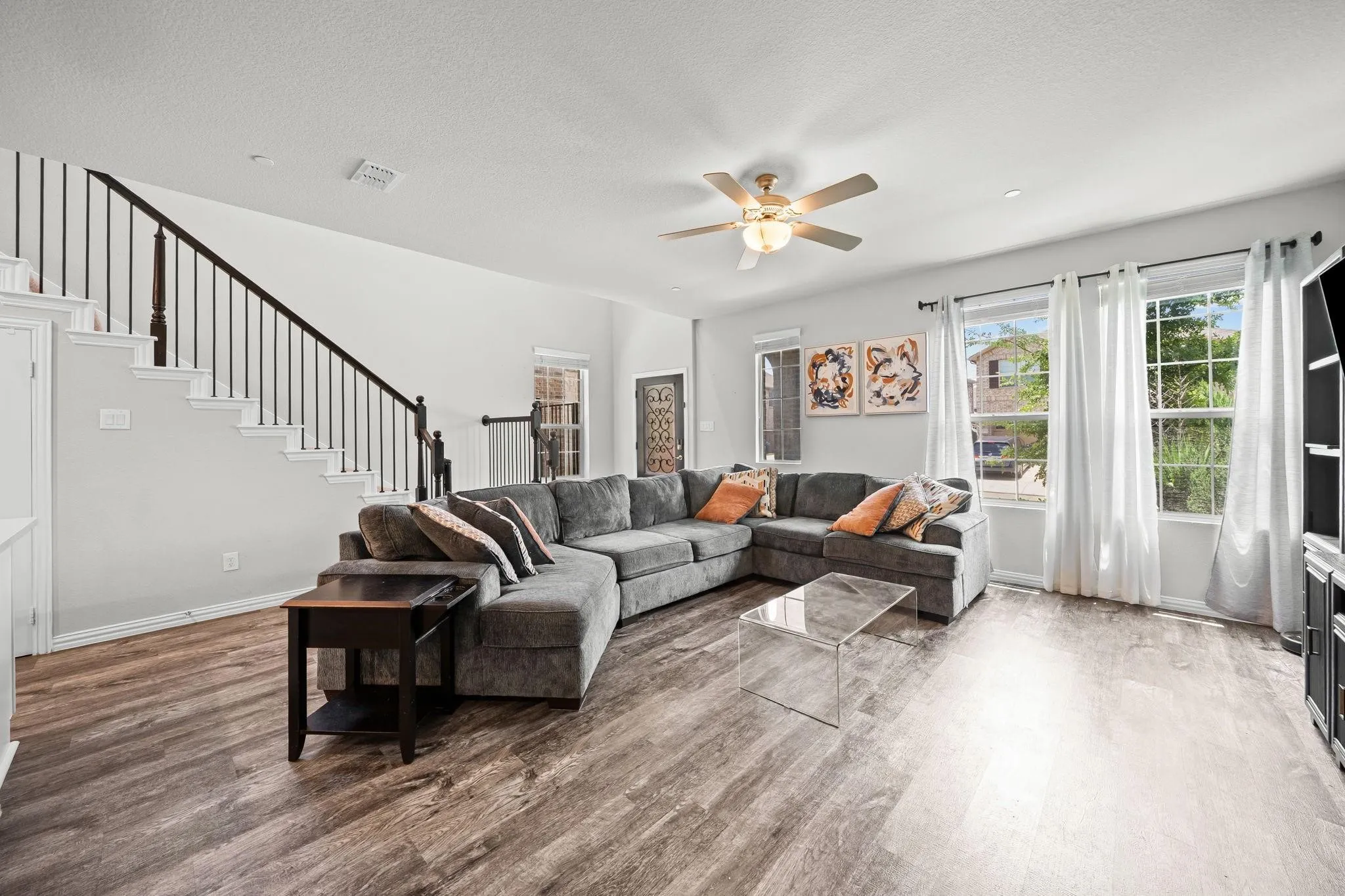 Spacious living area featuring wood-finish flooring, a ceiling fan with integrated lighting, and multiple windows
