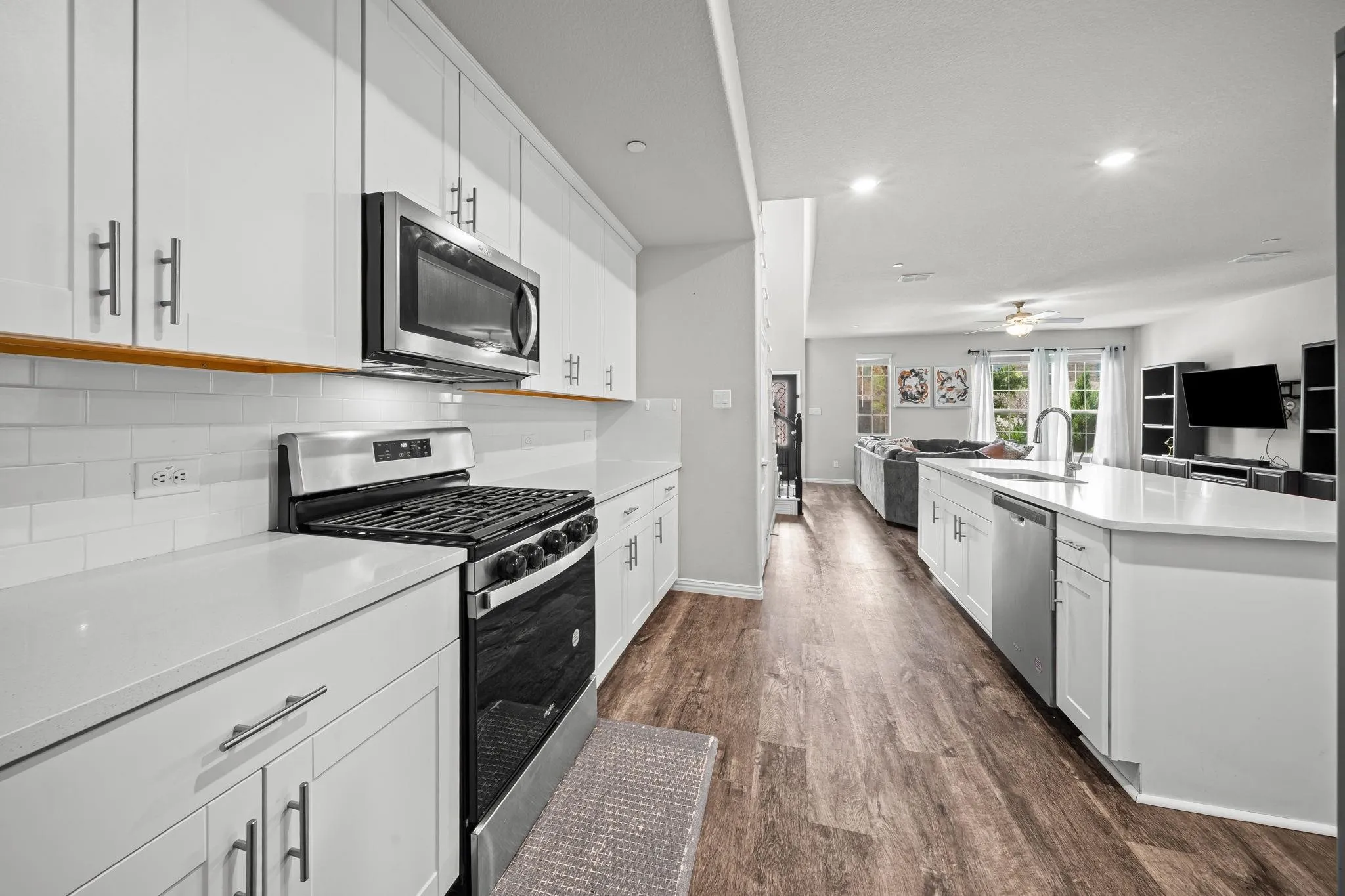 Modern kitchen featuring white cabinetry, stainless steel appliances, light countertops, subway tile backsplash, and wood-finish flooring