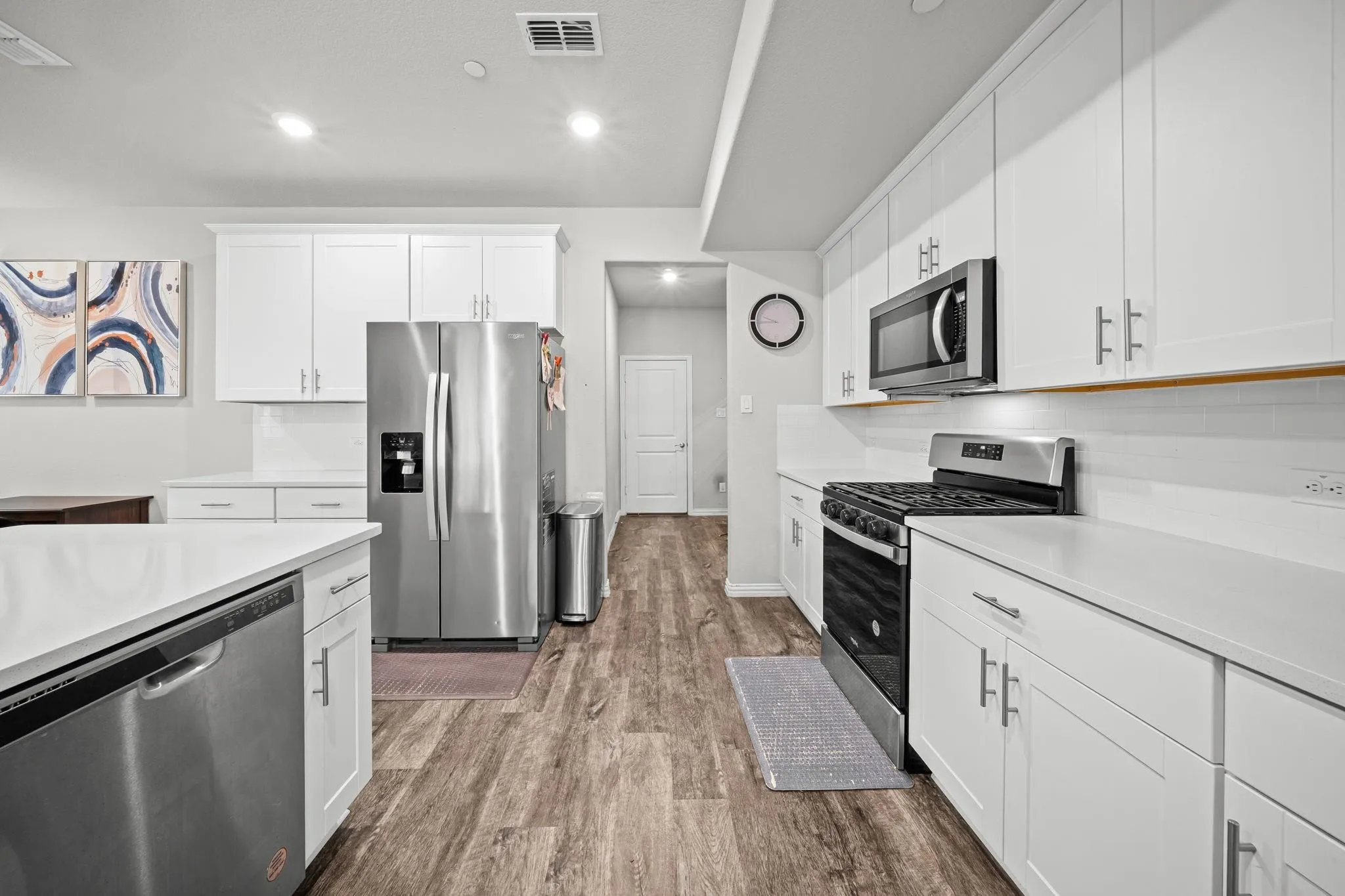 Kitchen featuring white cabinetry, stainless steel appliances, wood-finish flooring, white countertops, and a white subway tile backsplash