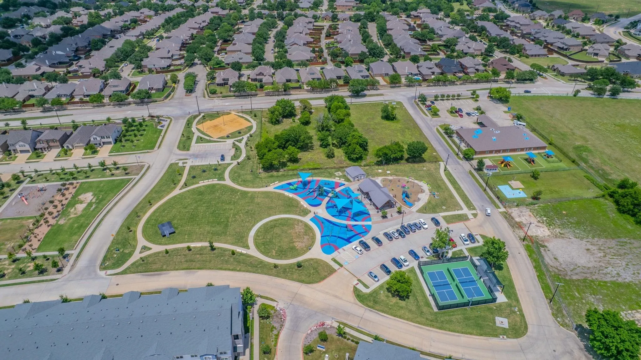 Community green space featuring a playground, walking paths, tennis courts, and a sand volleyball court