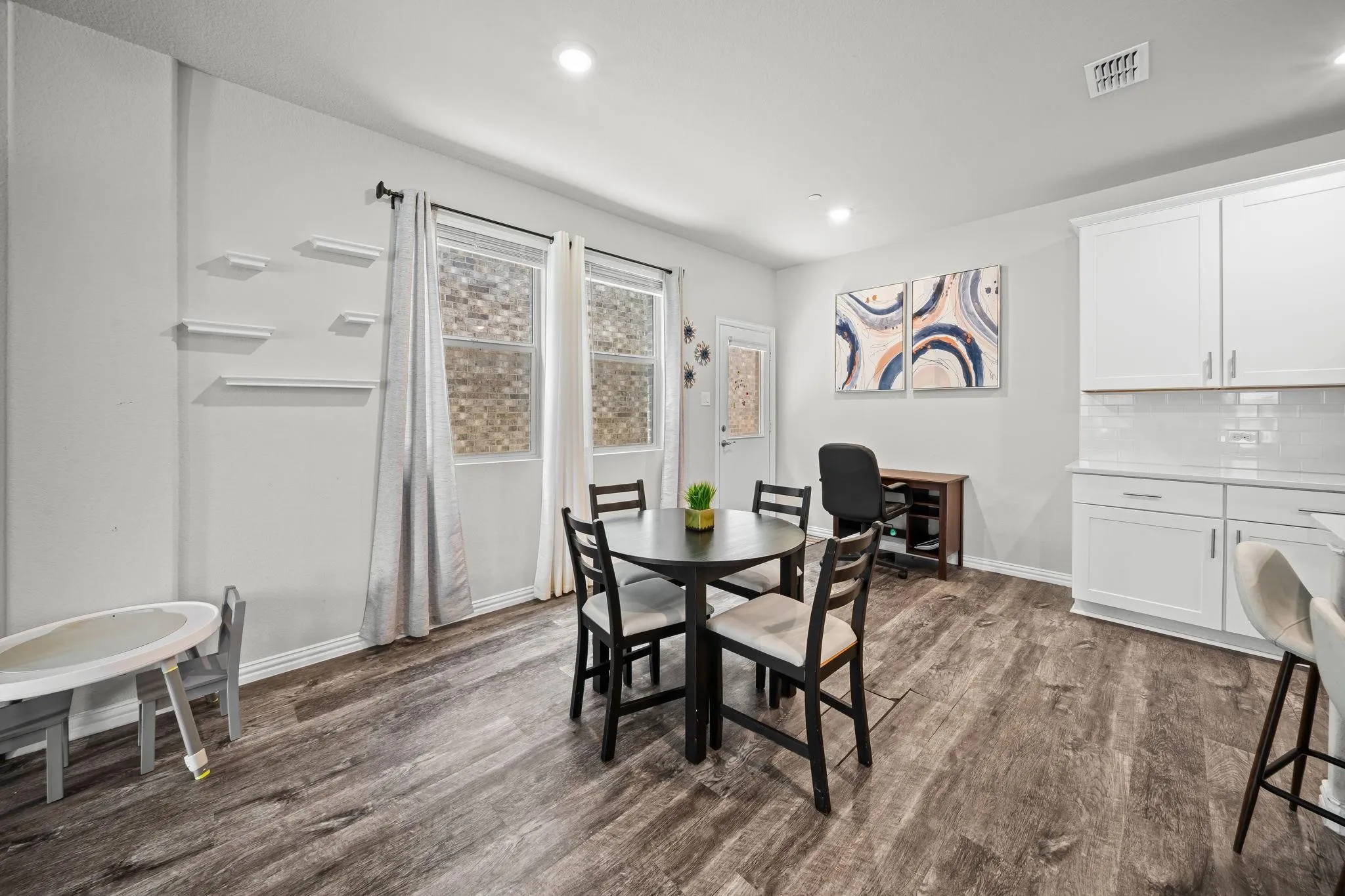 Wood-finish flooring, white cabinetry, light-colored walls, recessed lighting, and a kitchen backsplash