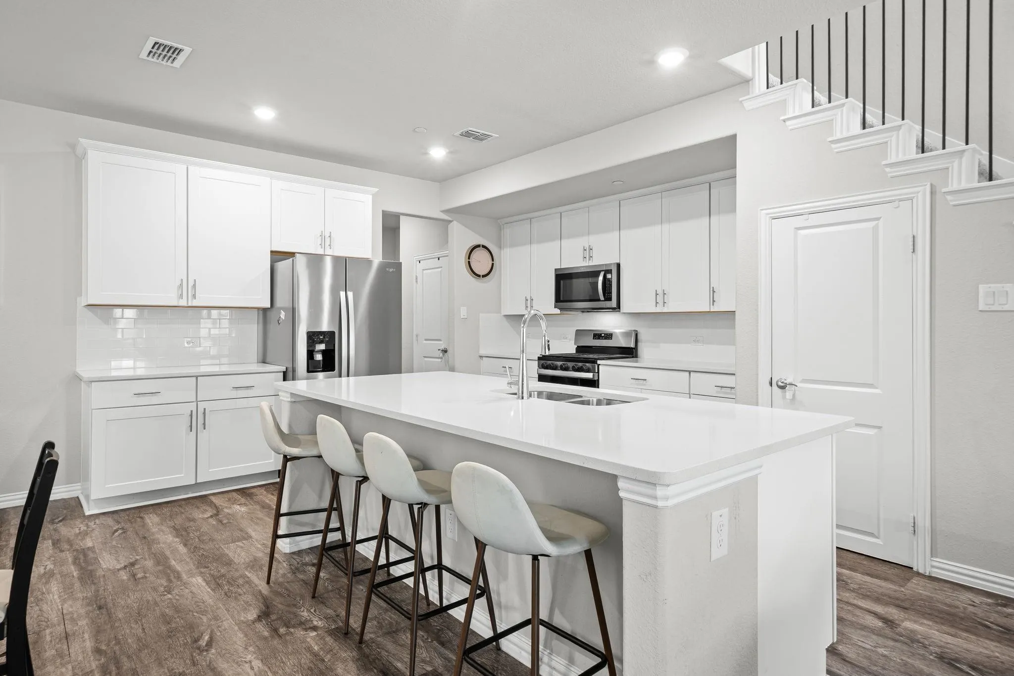 Contemporary kitchen featuring white cabinetry, stainless steel appliances, a center island with countertop seating, and wood-finish flooring