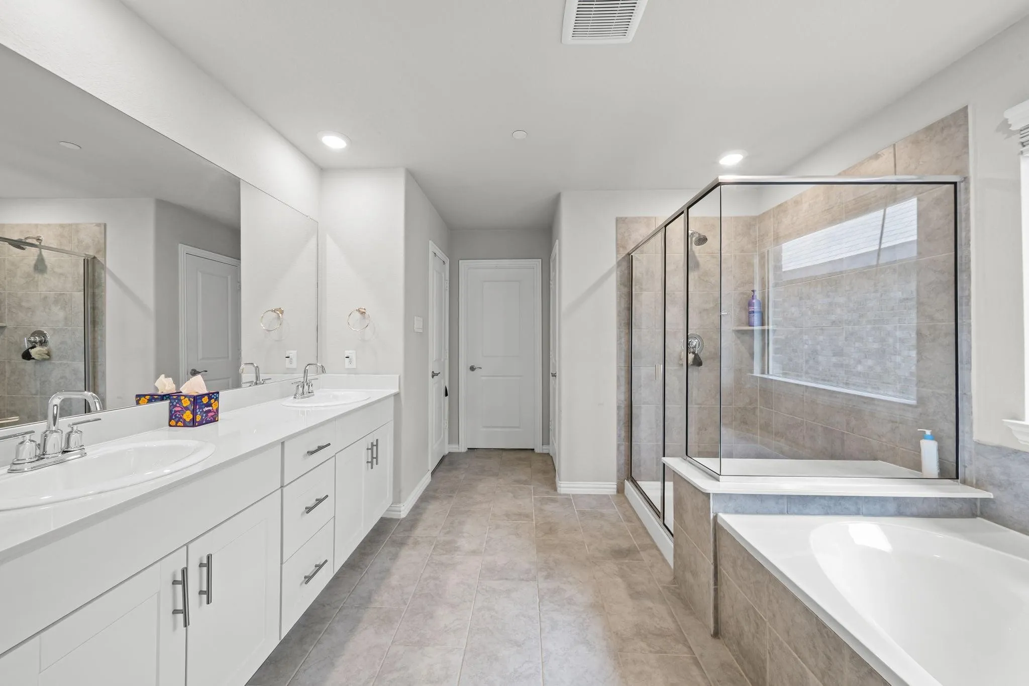 Dual vanity with undermount sinks, separate glass-enclosed shower, built-in bathtub, and tile flooring