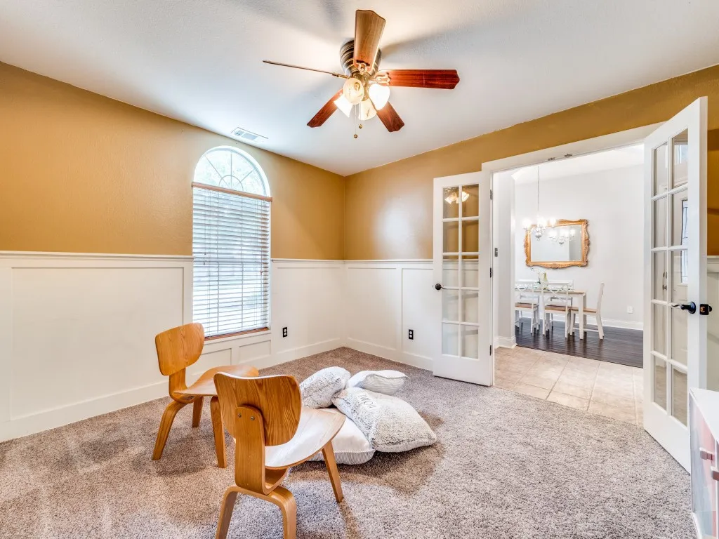 Arched window with blinds, ceiling fan, carpet flooring, wainscoting, and French doors with glass panels