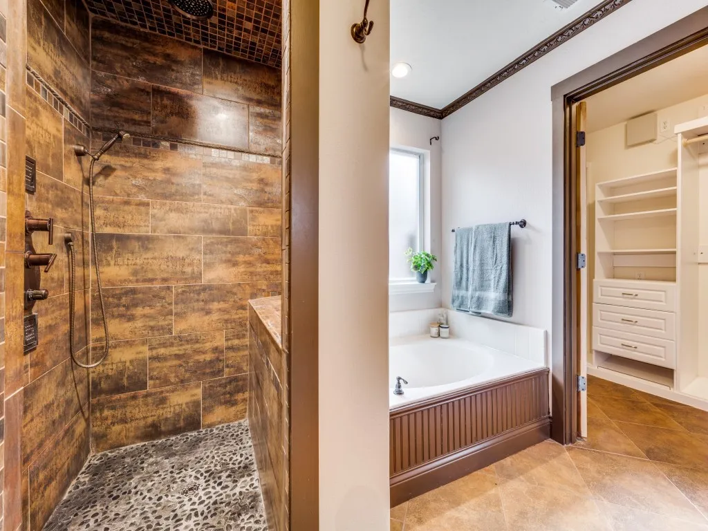 Walk-in shower with natural stone tile and pebble-stone flooring, featuring a built-in bench and a rain showerhead