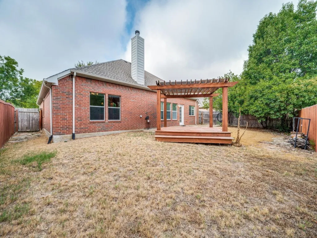 Brick exterior with a prominent chimney, wood-tone decking, and a coordinating pergola