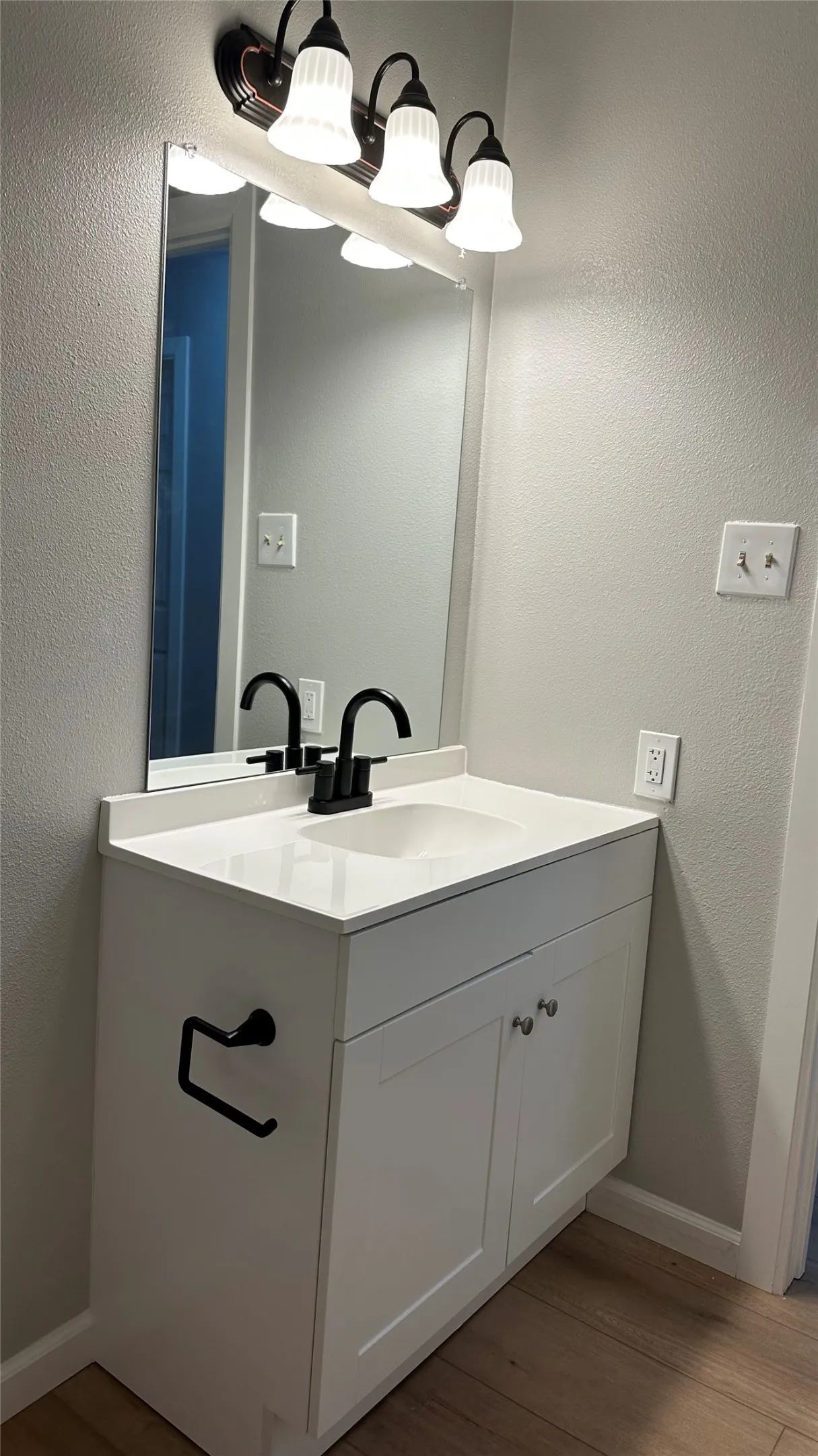 White vanity with shaker-style cabinet doors, integrated sink, and a black-finish faucet