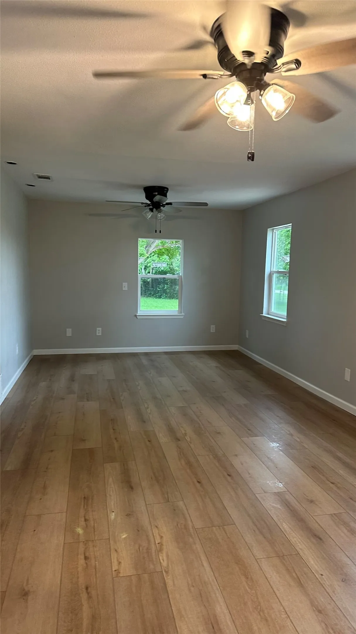 Wood-finish flooring, neutral wall tones, two ceiling fans with integrated lighting, and multiple windows