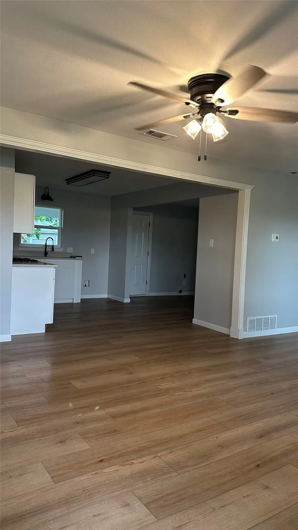 Wood-finish flooring throughout, white trim, and a ceiling fan with integrated lighting