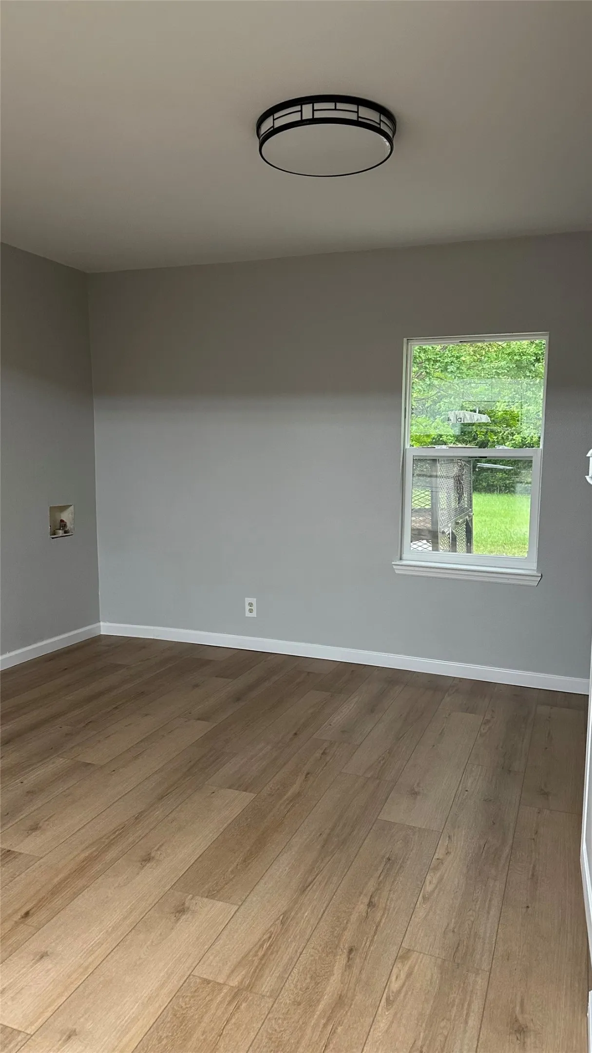 Wood-finish flooring, neutral gray wall paint, and a modern flush-mount ceiling light