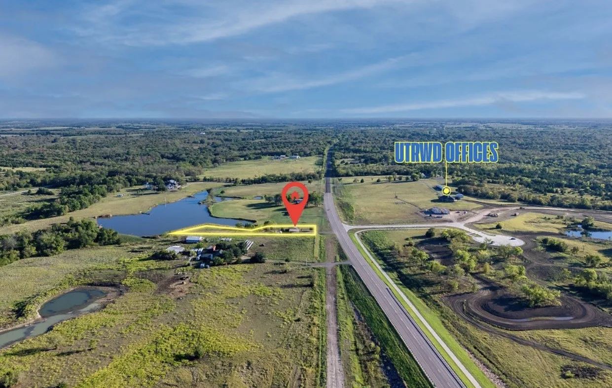 Expansive land parcel featuring a visible roadway, natural water body, and surrounding undeveloped terrain