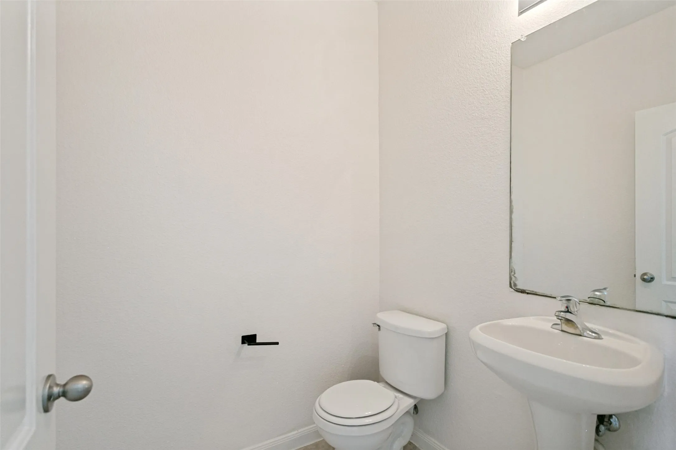 Powder room featuring a pedestal sink with chrome faucet, a white toilet, and a wall-mounted mirror