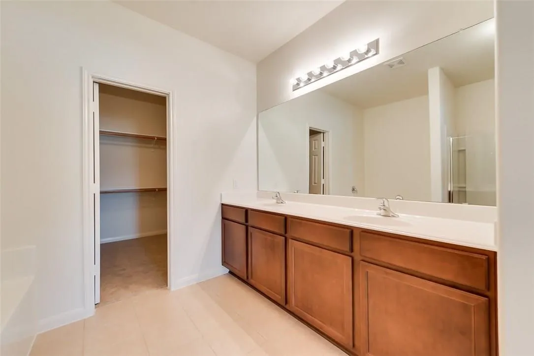 Double vanity featuring dual sinks, a large mirror, and ample wood-finish cabinetry