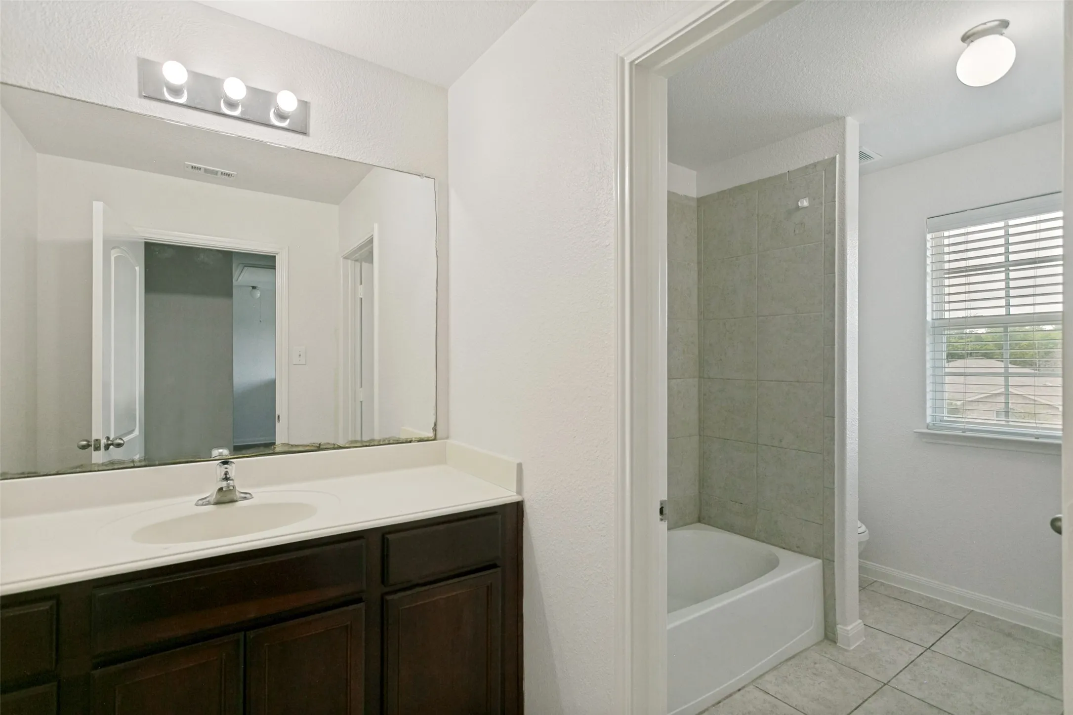 Bathroom featuring a dark wood-finish vanity with an integrated sink, a large wall-mounted mirror, and a three-bulb vanity light fixture