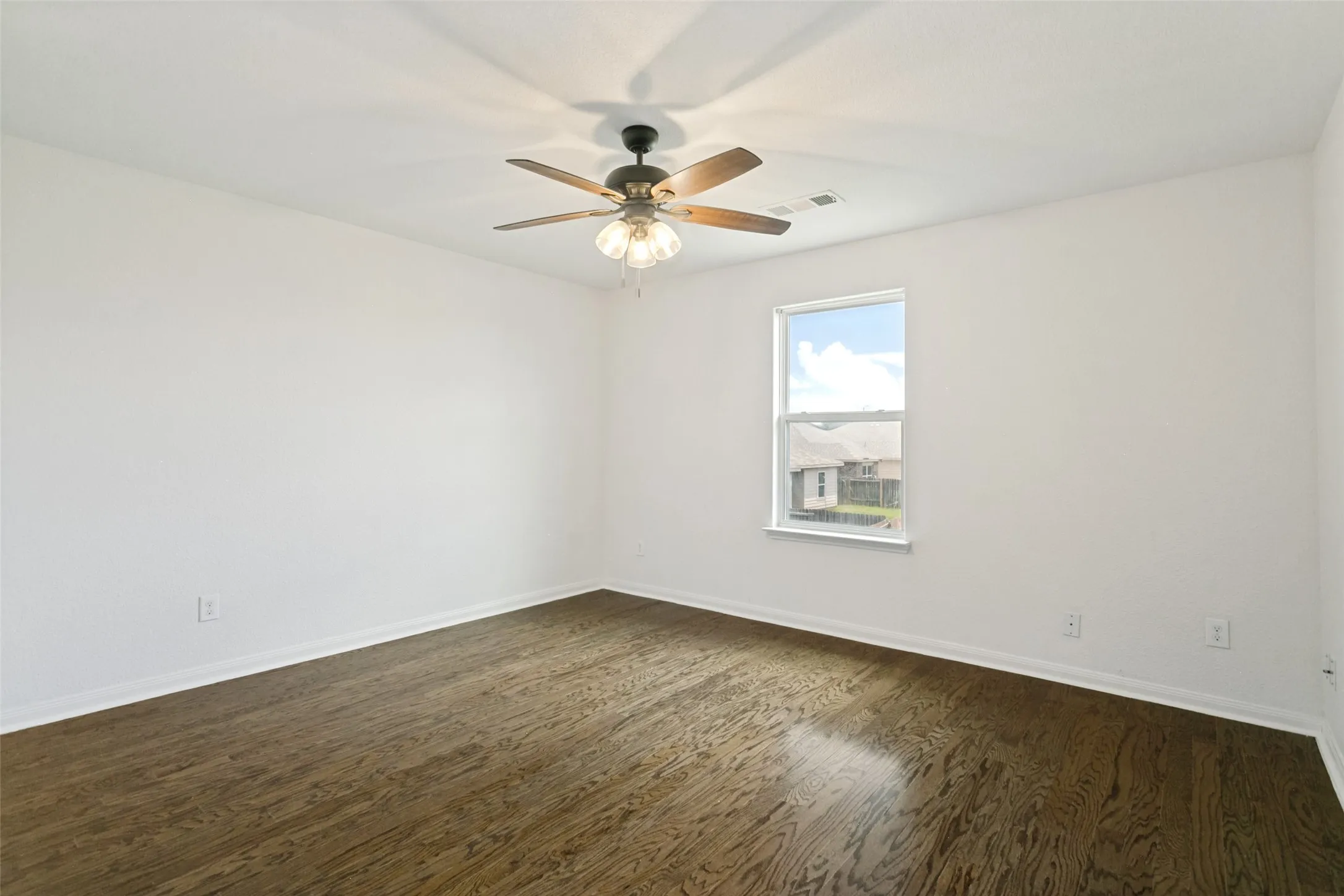 Spacious room featuring wood-finish flooring, white baseboards, and a ceiling fan with integrated lighting