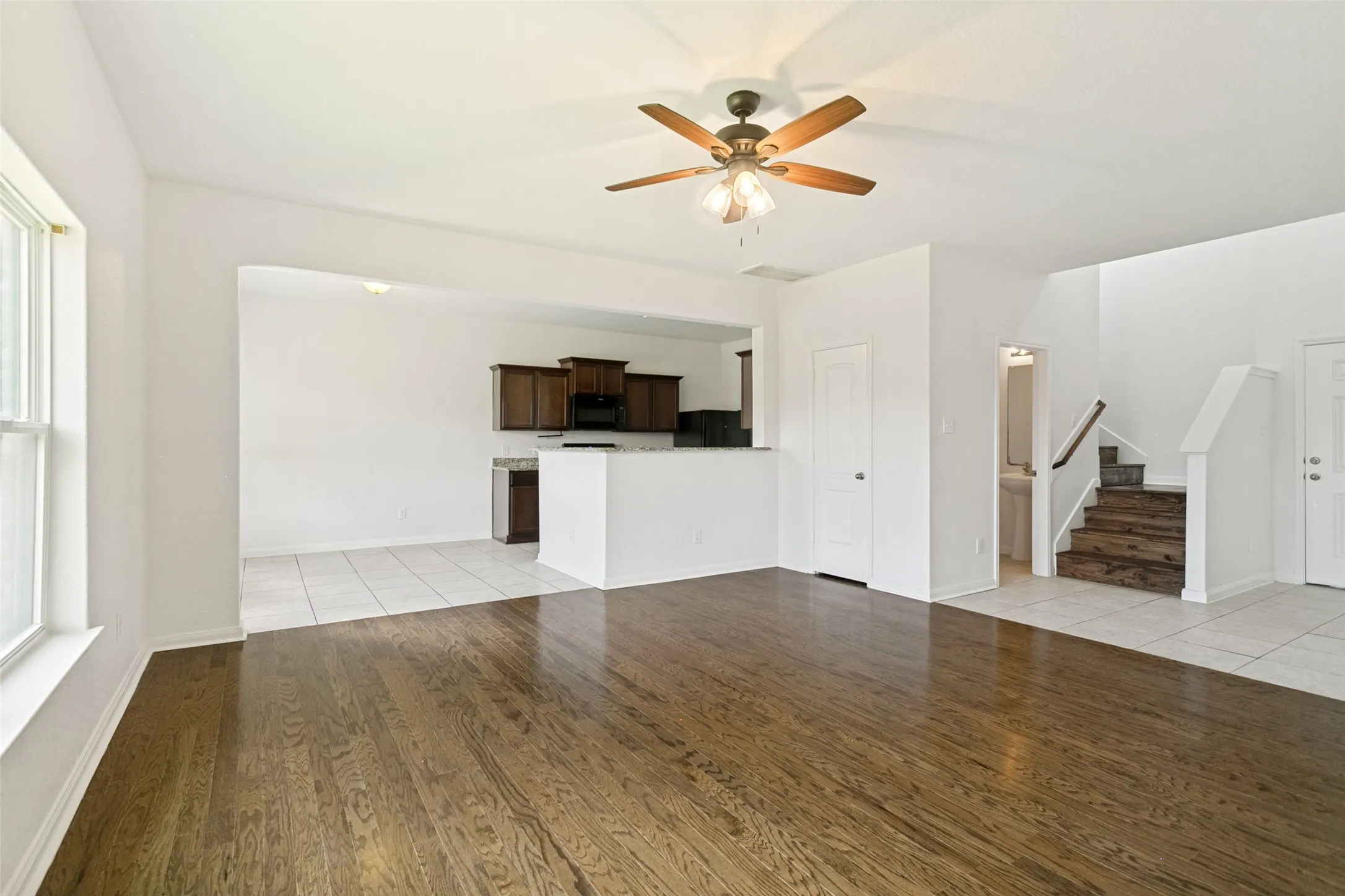Spacious living area featuring wood-finish flooring, a ceiling fan with integrated lighting, and an open concept layout to the kitchen