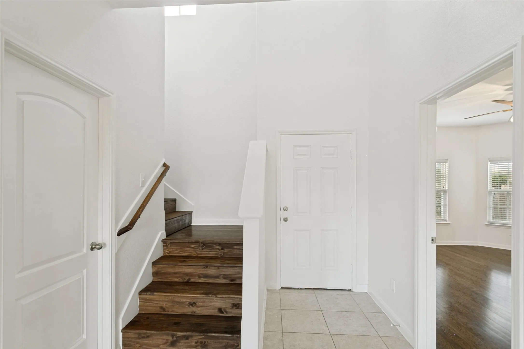 Entry foyer featuring light-toned tile flooring, a staircase with wood-finish treads and a matching handrail, and high ceilings with upper-level windows