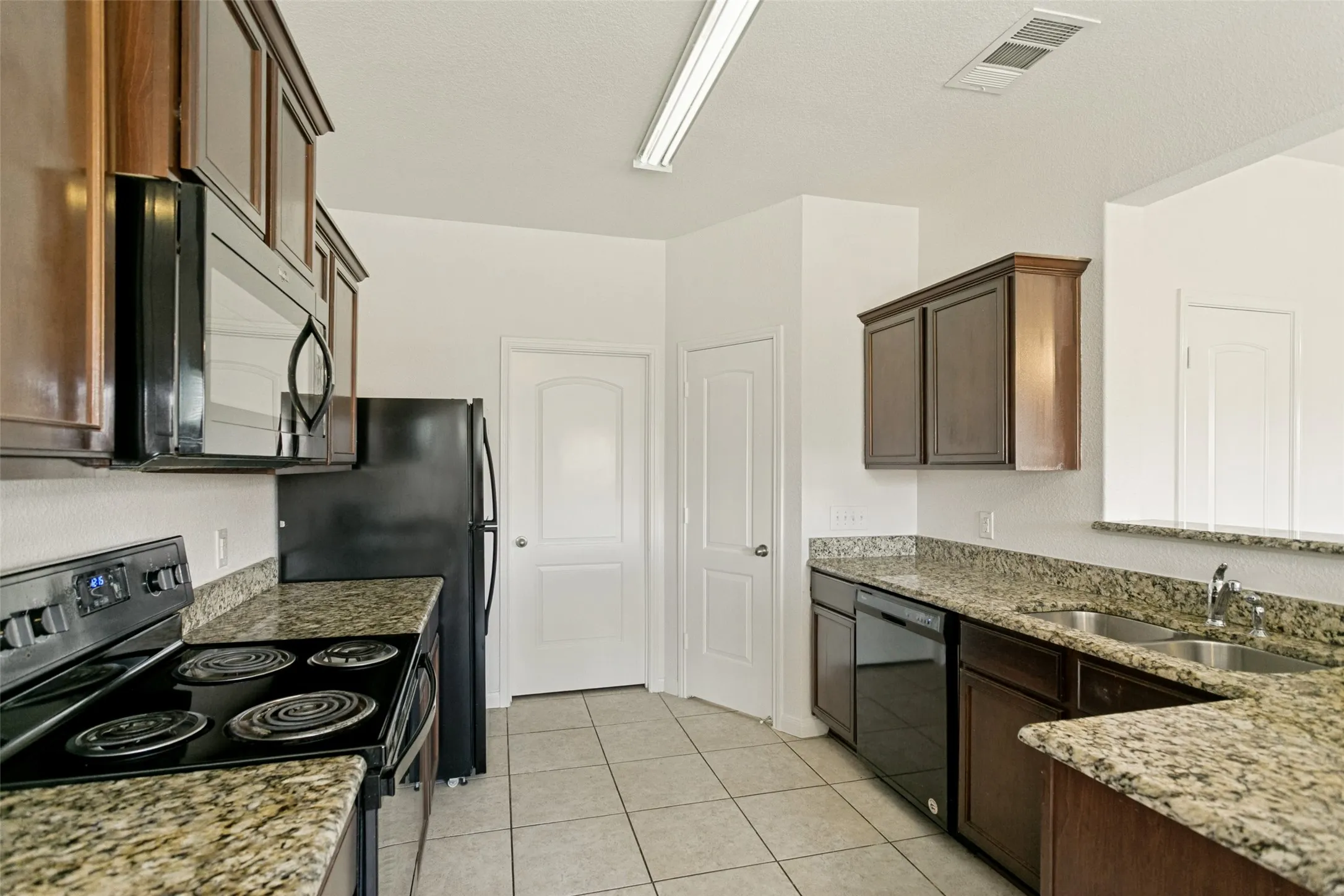 Kitchen featuring black appliances, granite countertops, wood-finish cabinetry, tile flooring, and a double-basin sink